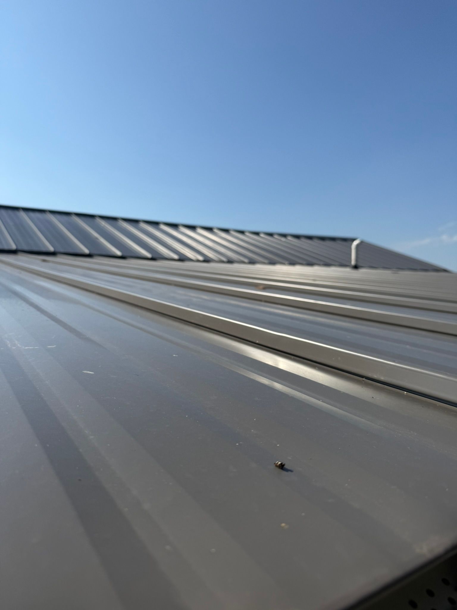 Gray metal roof with ridges against a blue sky.