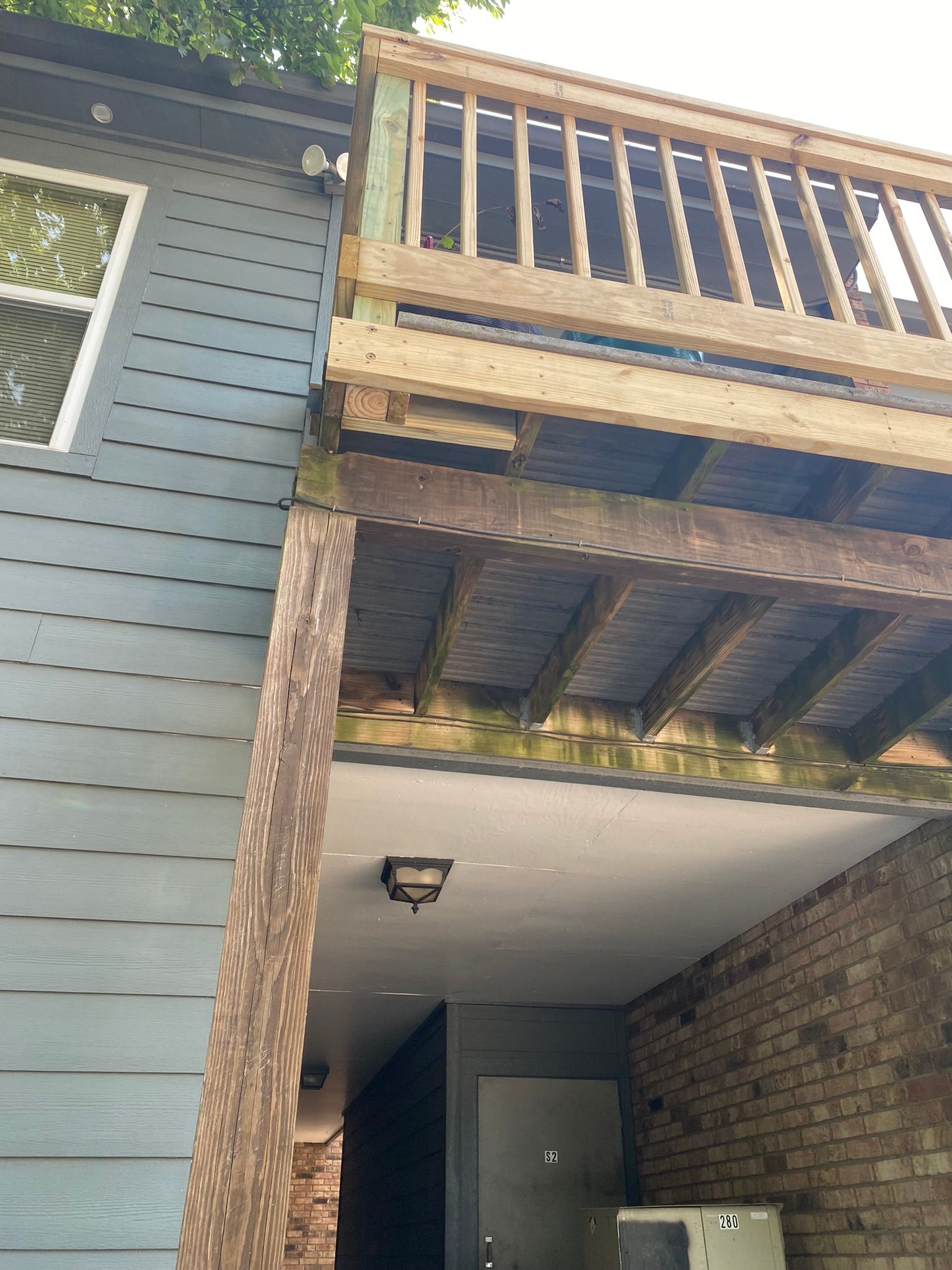 Low-angle view of a wooden deck attached to a gray-sided building; a brick column supports the deck.