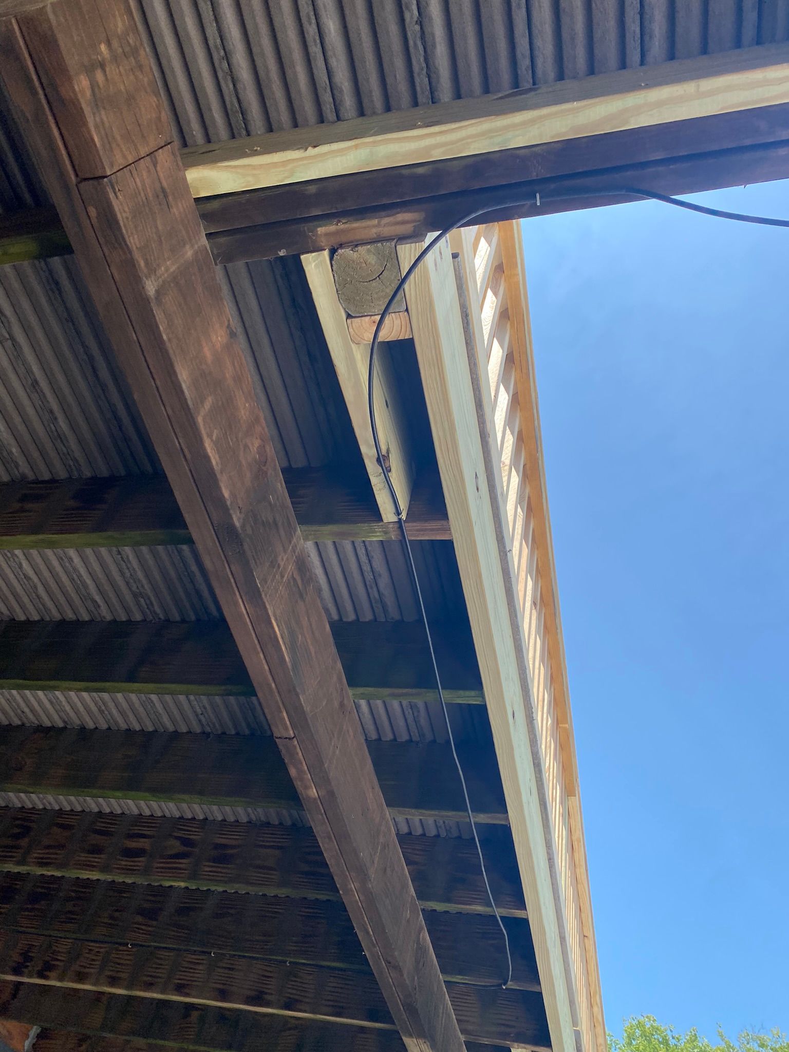 View from below of a weathered wooden roof and gutter under a clear blue sky.