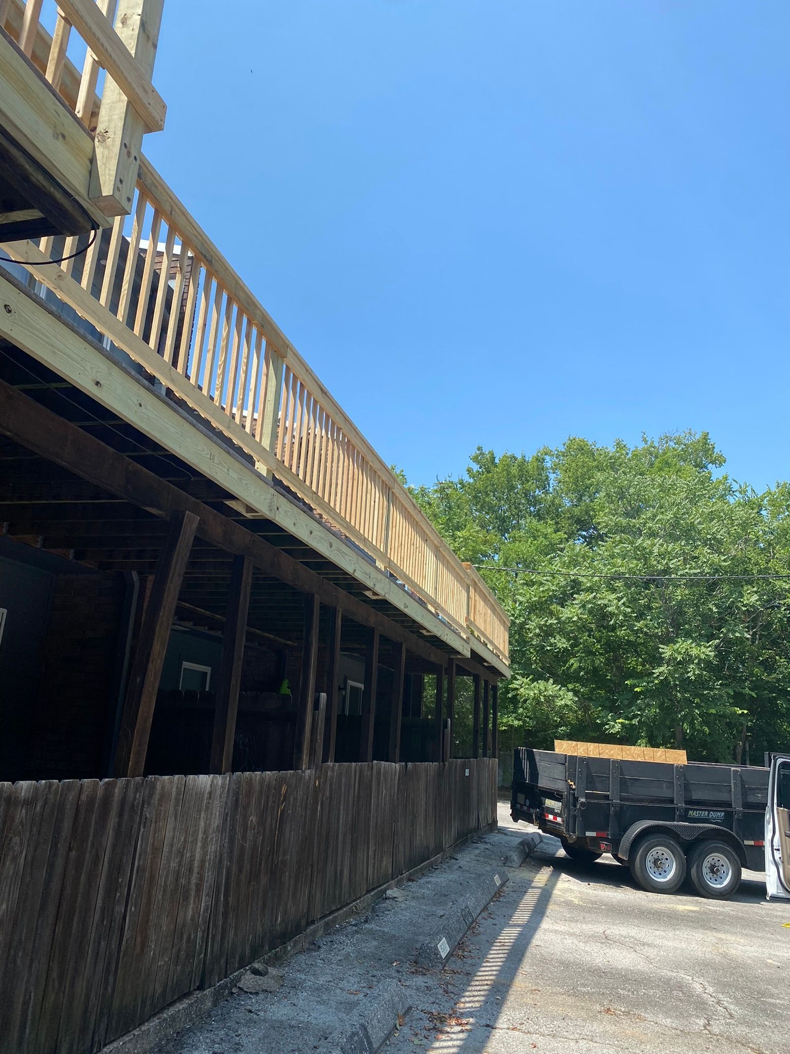Wooden deck under construction with railing, against a blue sky, trailer to the right.