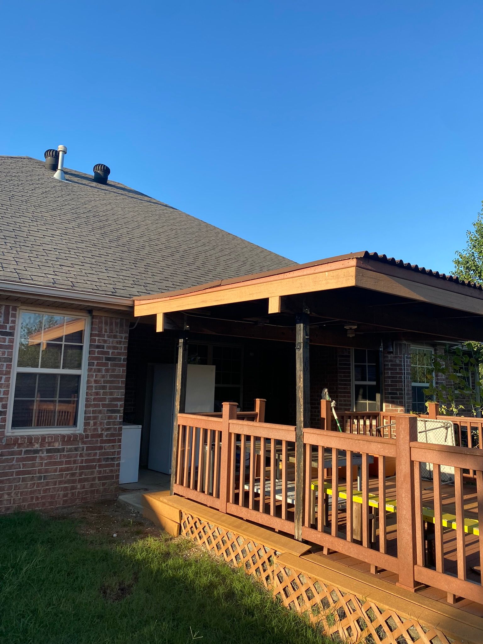 Brick house exterior with wooden deck, railings, and covered patio under a blue sky.