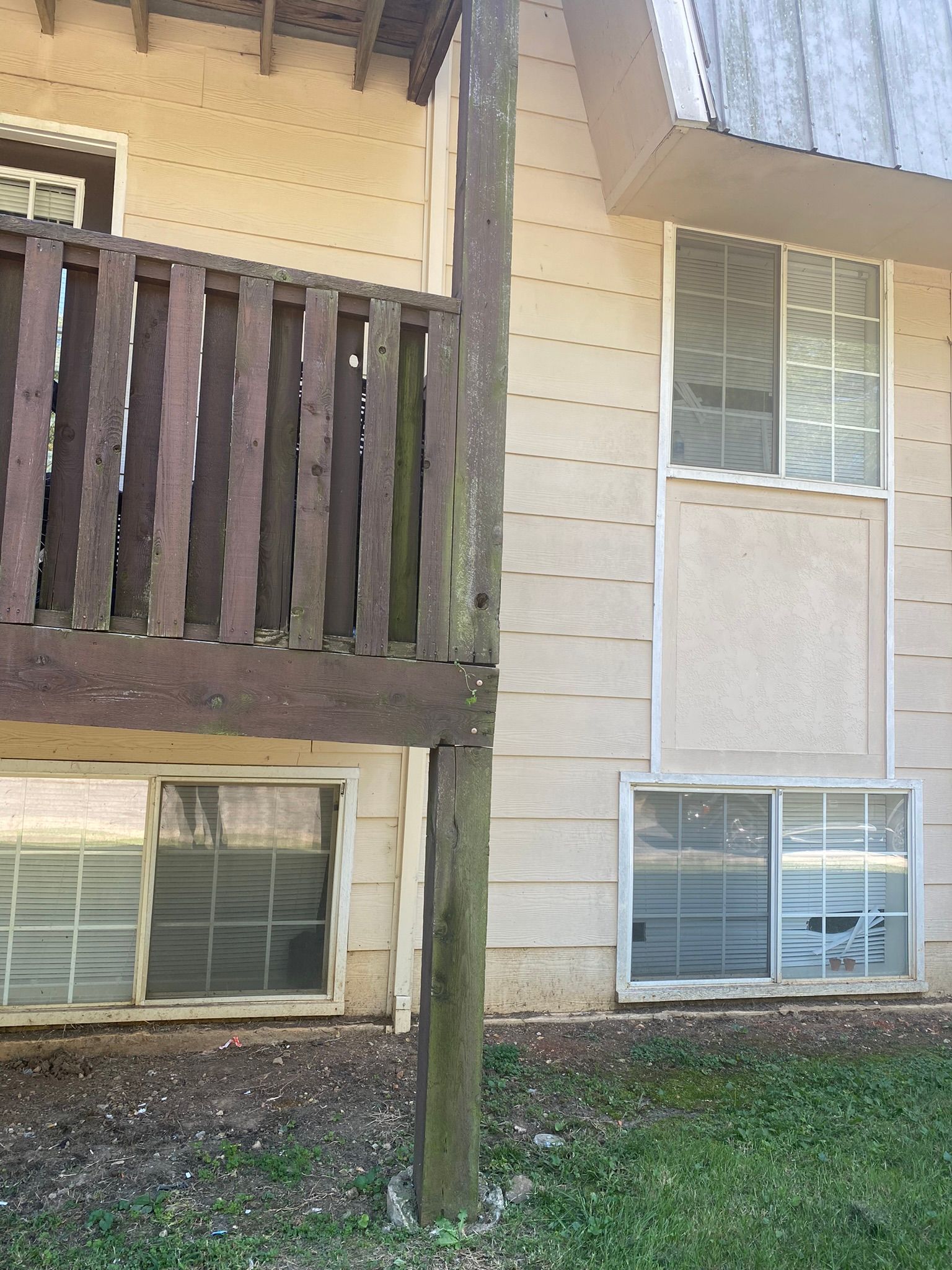 Exterior view of a building with a wooden deck and several windows. The siding is beige. The deck is brown.