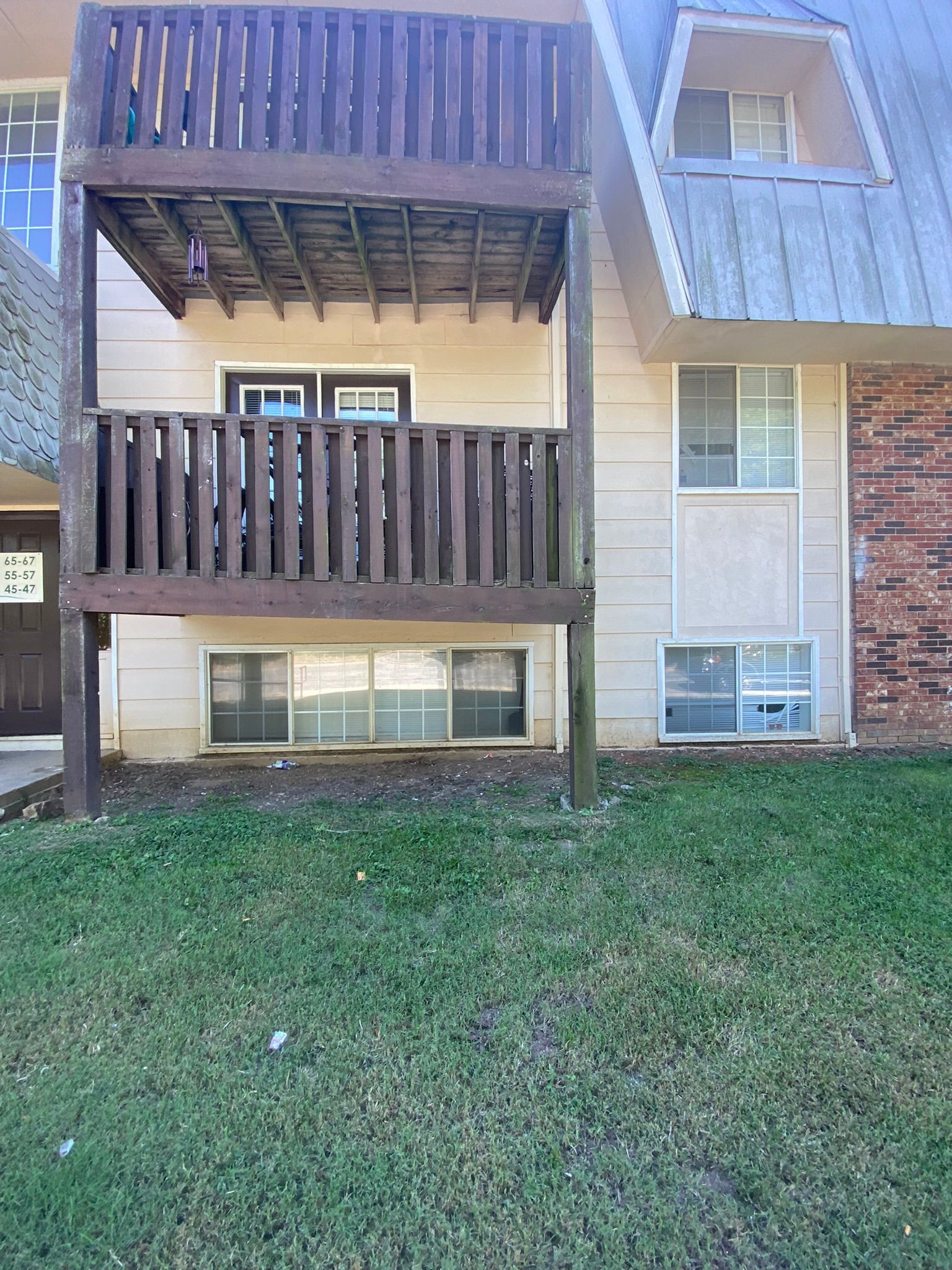 Two-story building with a wooden balcony. Green lawn in foreground. Beige exterior with windows.
