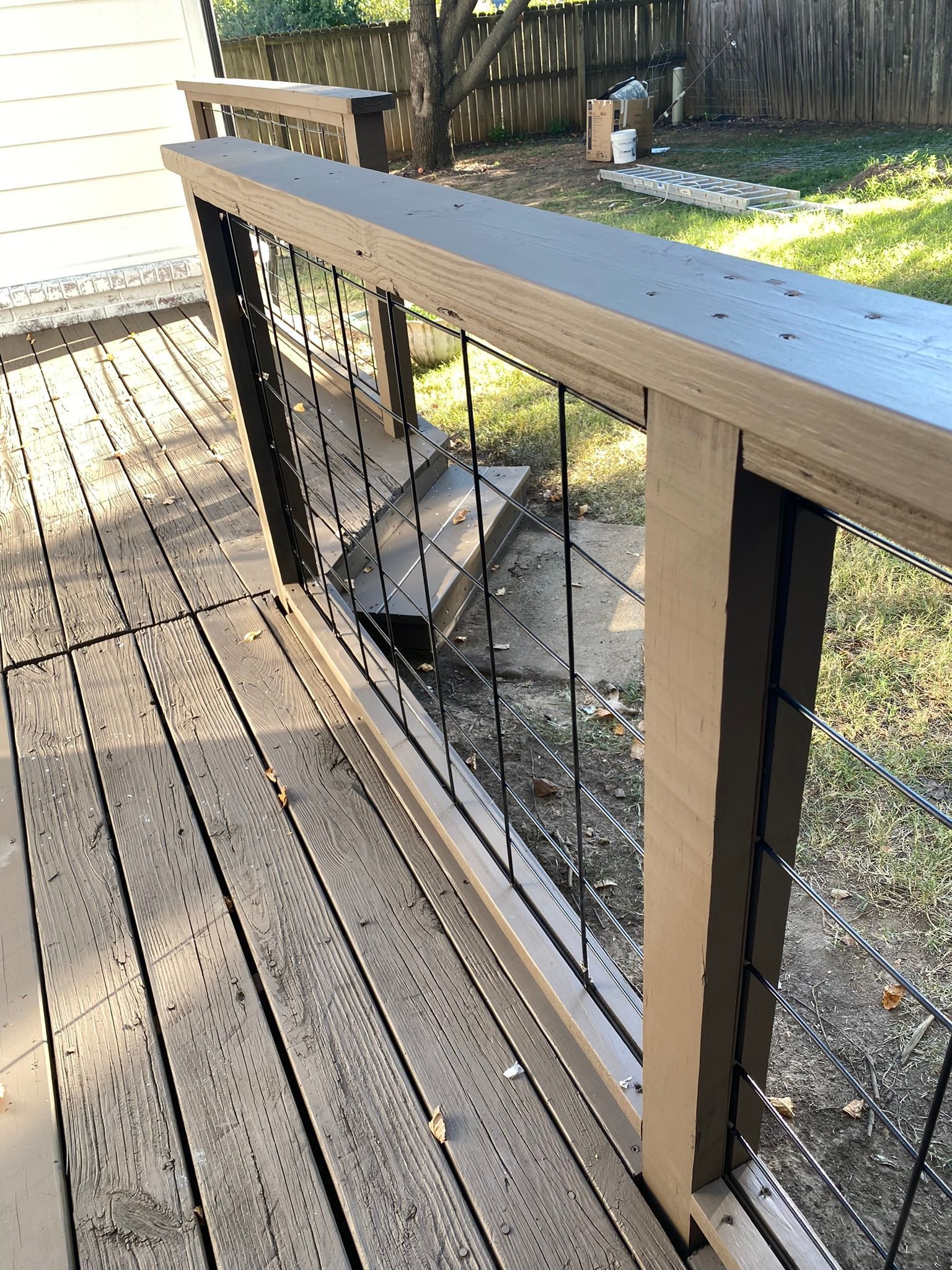 Wooden deck with brown and black railing, wire mesh infill, and a glimpse of backyard.