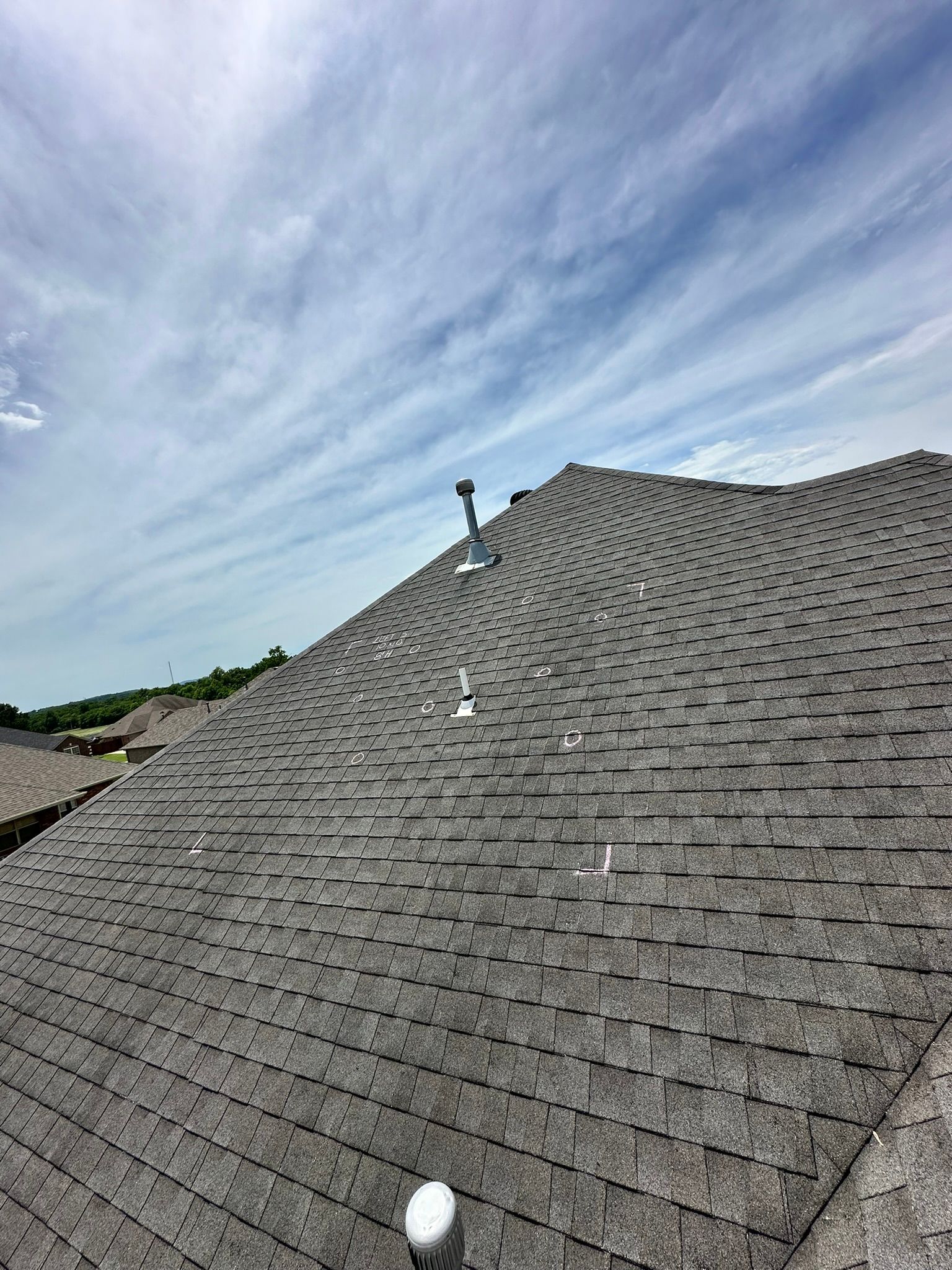Gray asphalt shingle roof with vents against a cloudy blue sky.