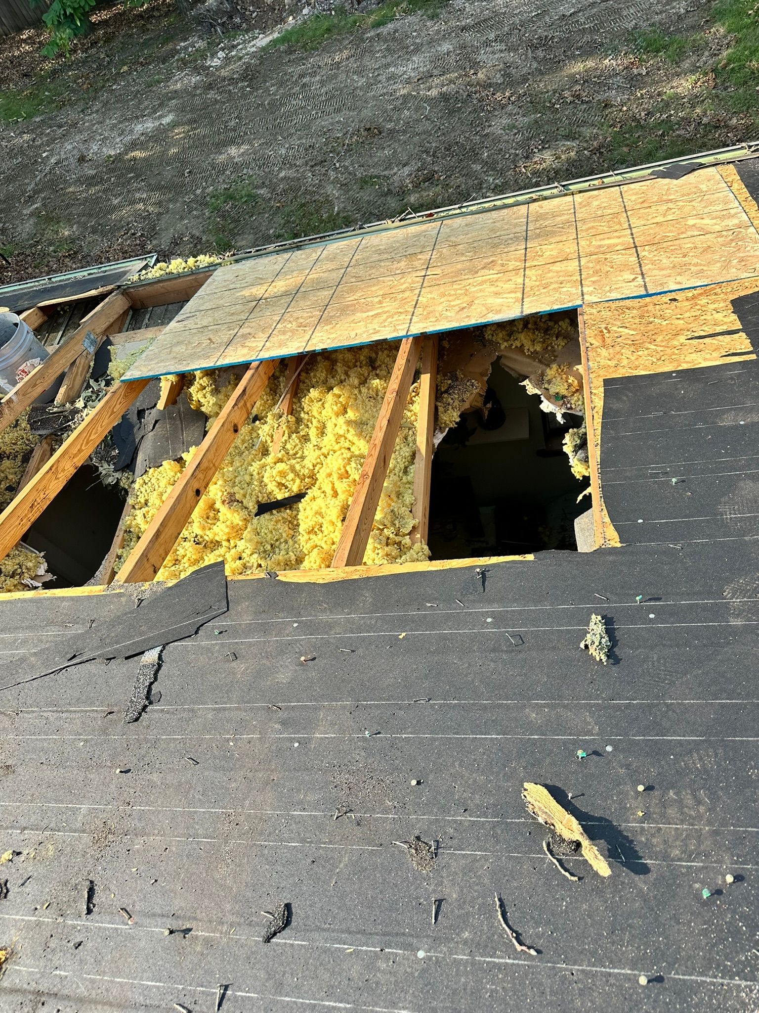 Damaged roof with hole exposing insulation and supporting beams.