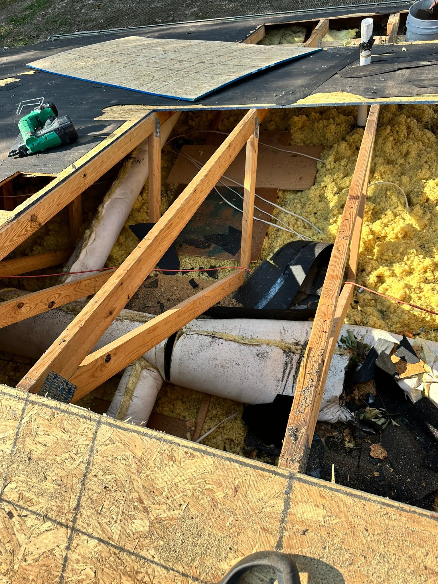 Roof partially open, exposing wood beams, insulation, and plumbing pipes. Green power tool visible.