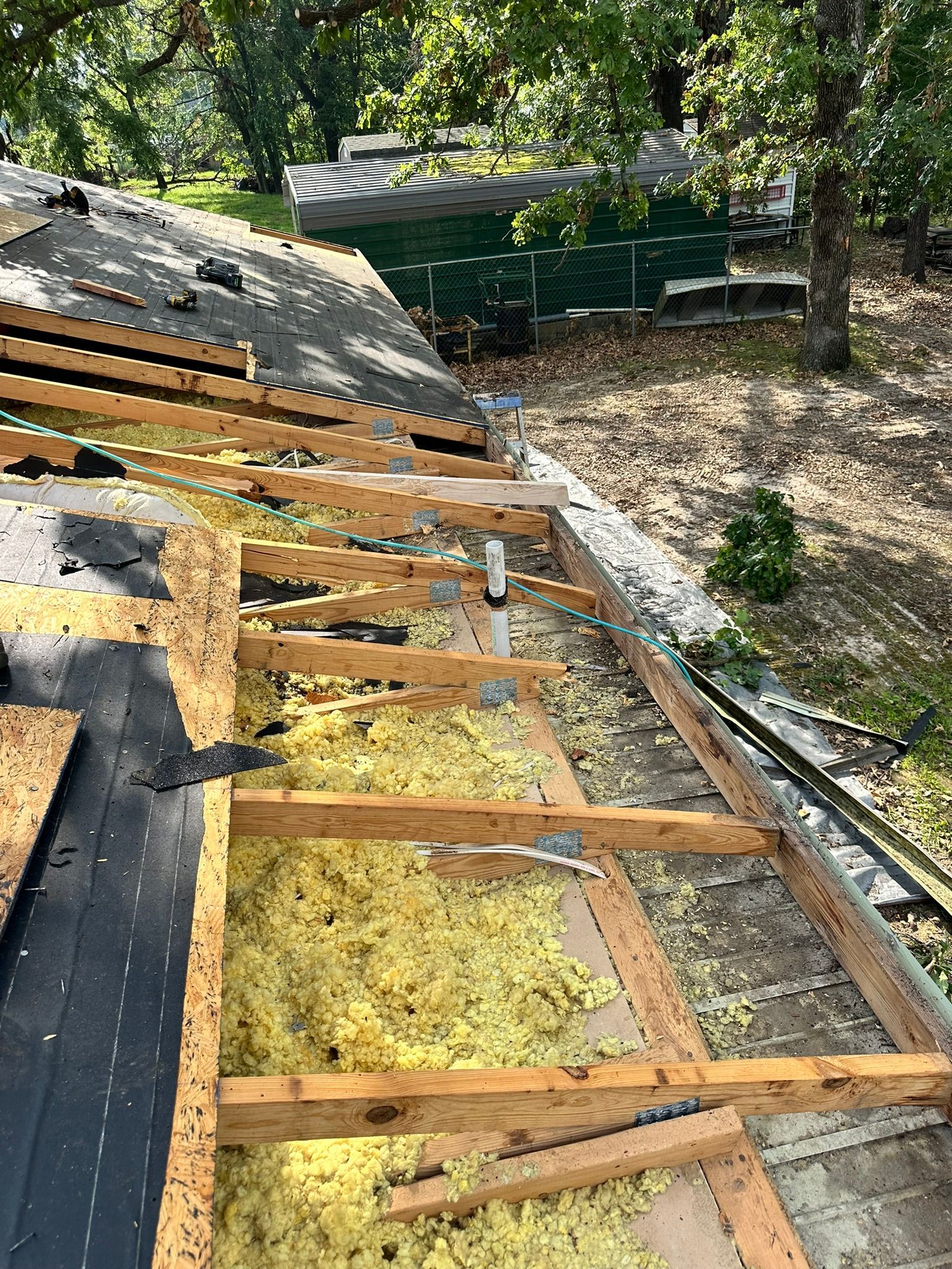 Roof under construction with exposed rafters, insulation, and partially laid roofing materials.