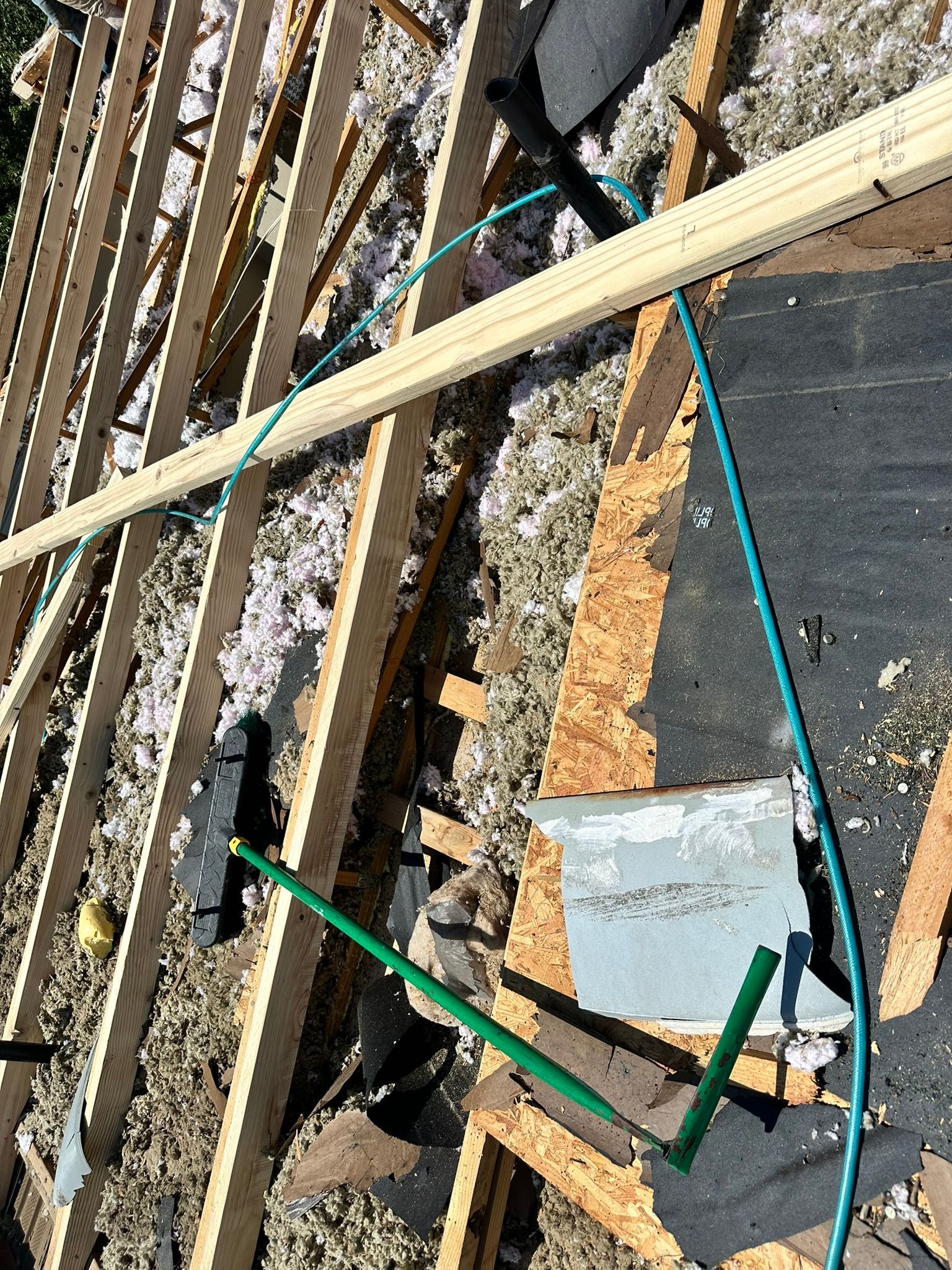 Overhead view of a roof under construction. Wooden beams, insulation, and a blue pipe are visible.