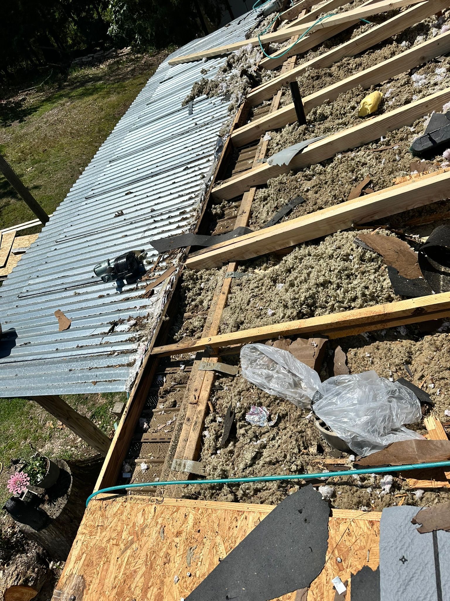 Roof partially dismantled; metal panels, insulation, and wooden structure exposed, outdoors.