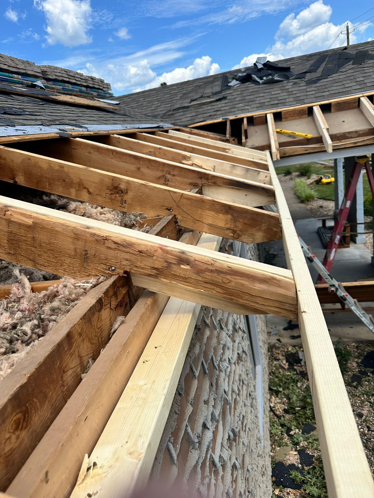 Roof partially dismantled, showing exposed rafters. Construction site with blue sky in background.