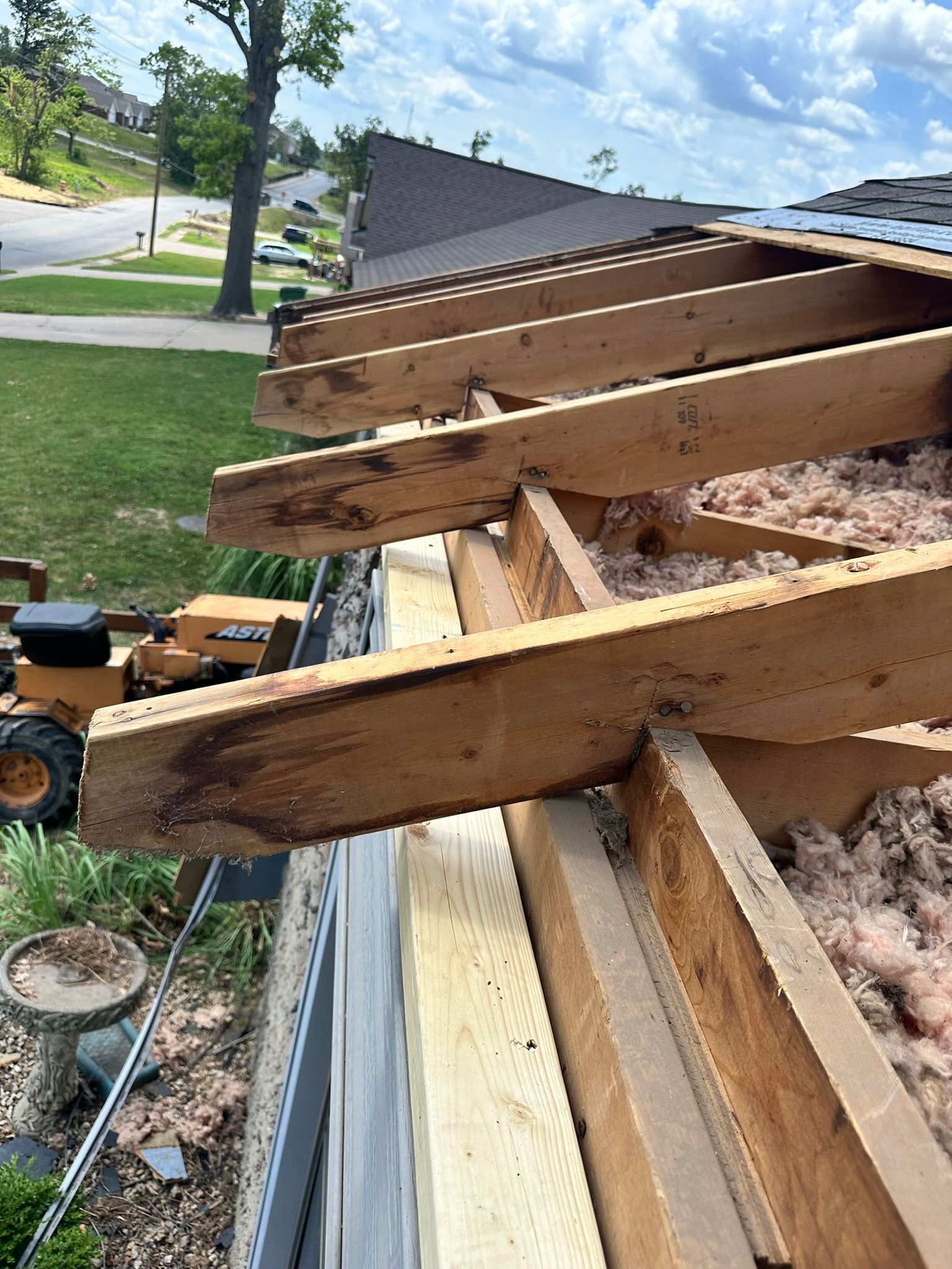 Roof construction in progress, showing exposed rafters, insulation, and a yellow tractor in the background. Blue sky overhead.