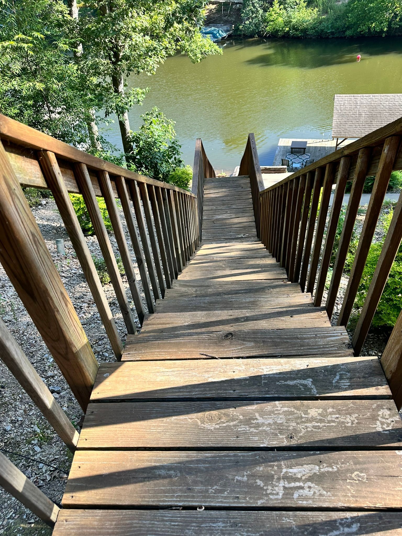 Wooden stairs lead down to a lake, flanked by railings. Sunlight casts shadows on the steps.