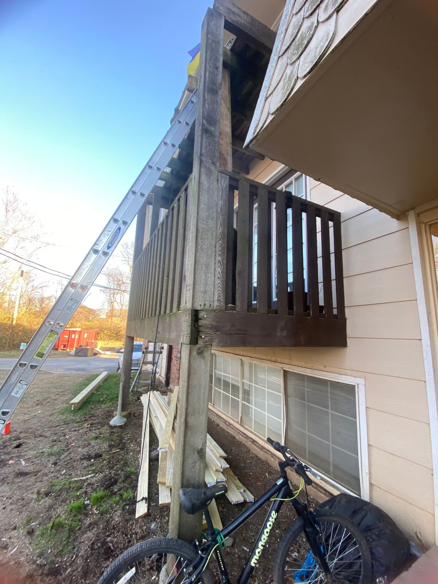 Exterior of building with ladder. Wooden balcony, bicycle, and peeling siding.
