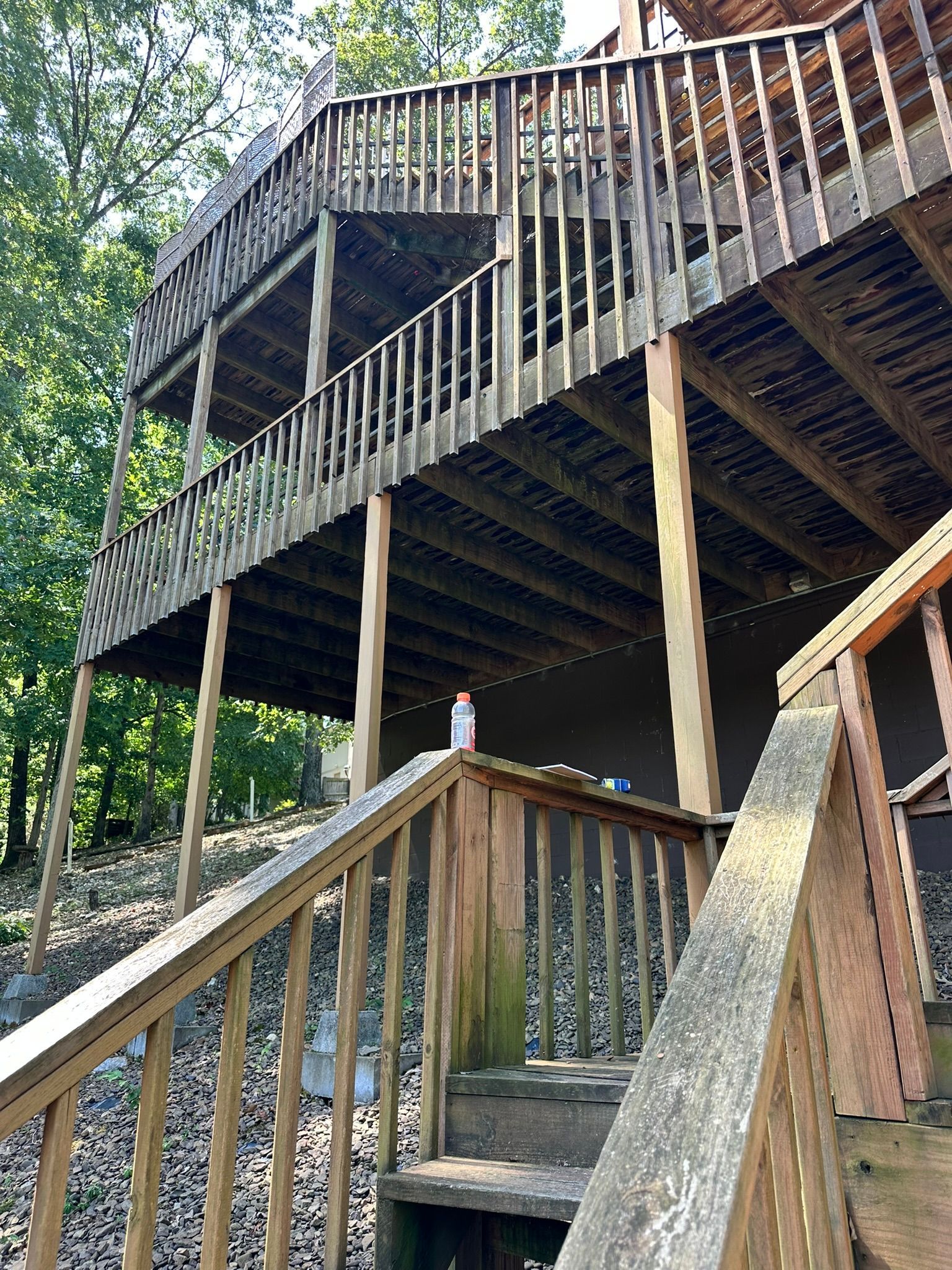 Wooden multi-level deck with stairs in a wooded area.