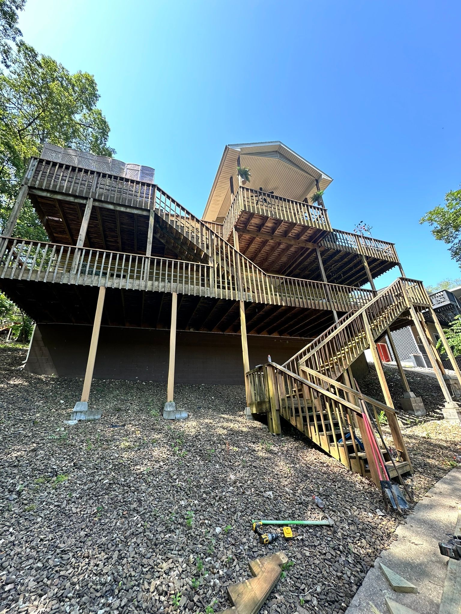 Multi-level wooden deck structure with stairs, supported by posts, against a blue sky.