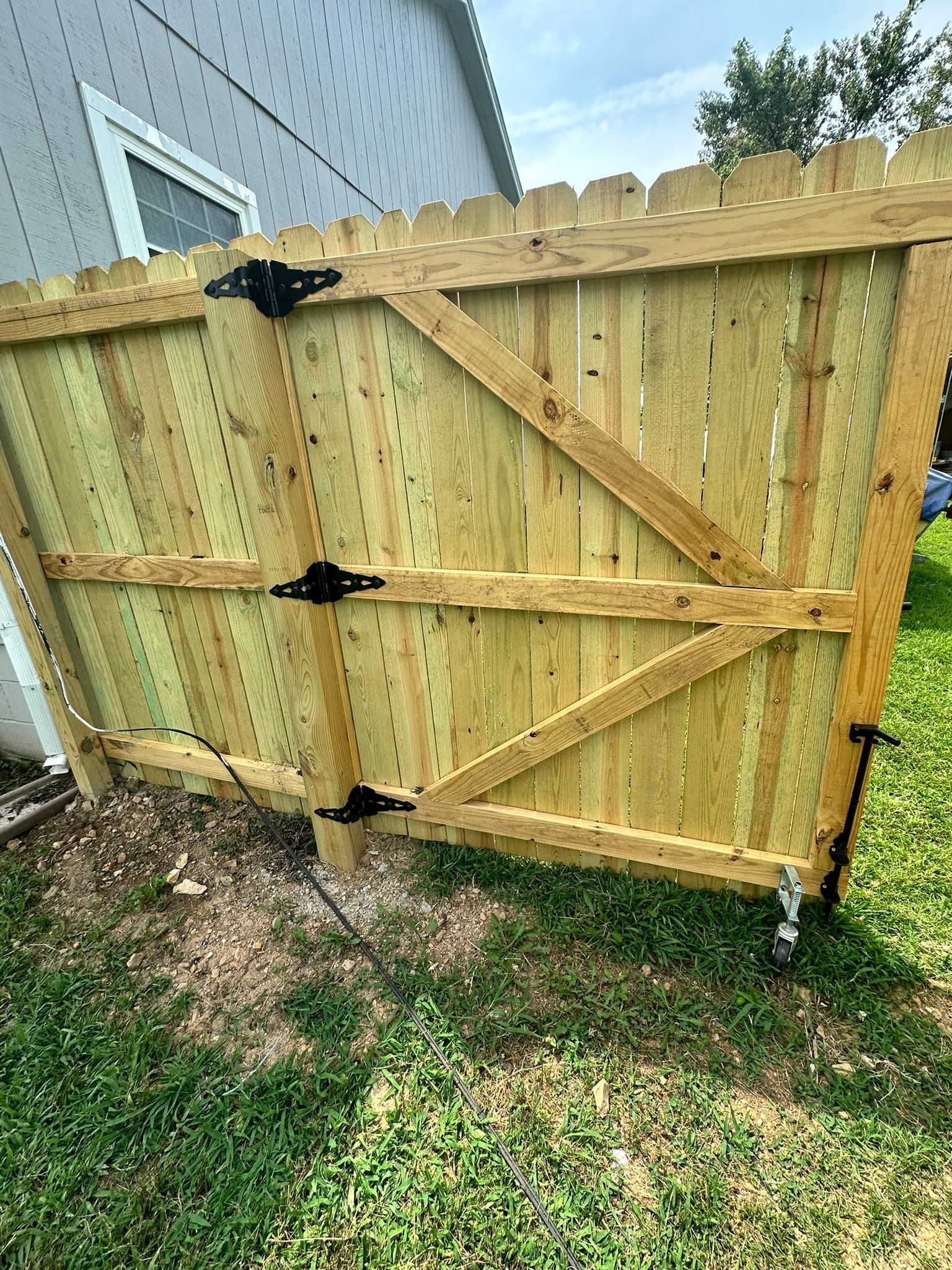 Wooden gate with black hinges and a diagonal brace, set in a backyard.