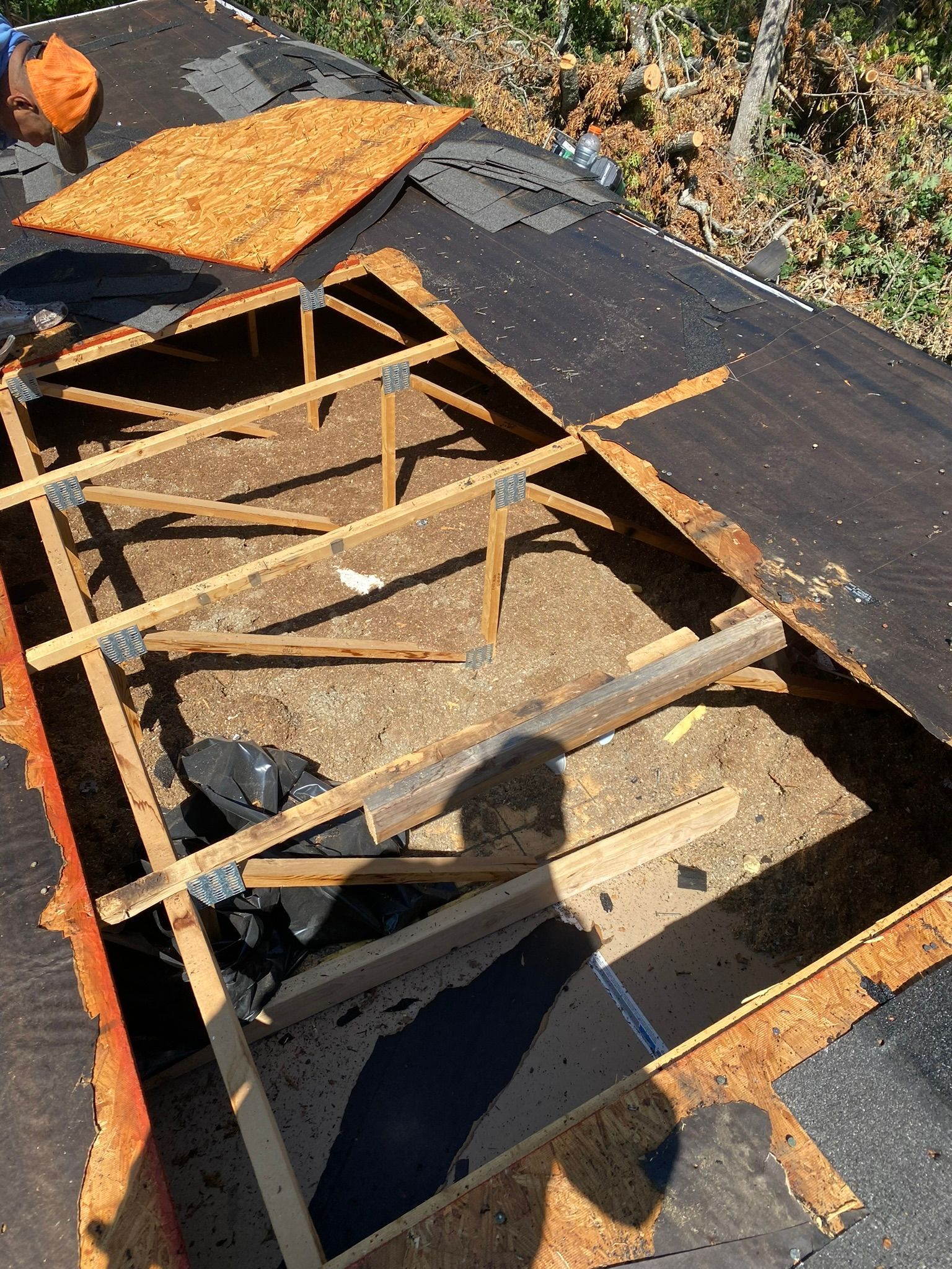 Overhead view of a roof with a large, open section revealing exposed wooden supports and debris.