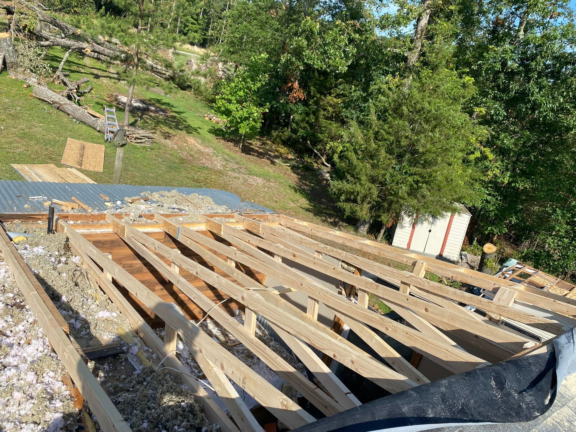 Roof under construction, showing wooden beams, insulation, and building materials, outdoors.