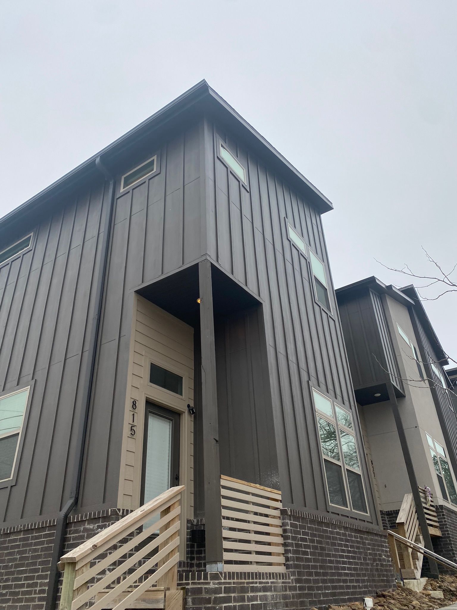 Modern townhome with dark brown siding, brick base, and wooden steps.