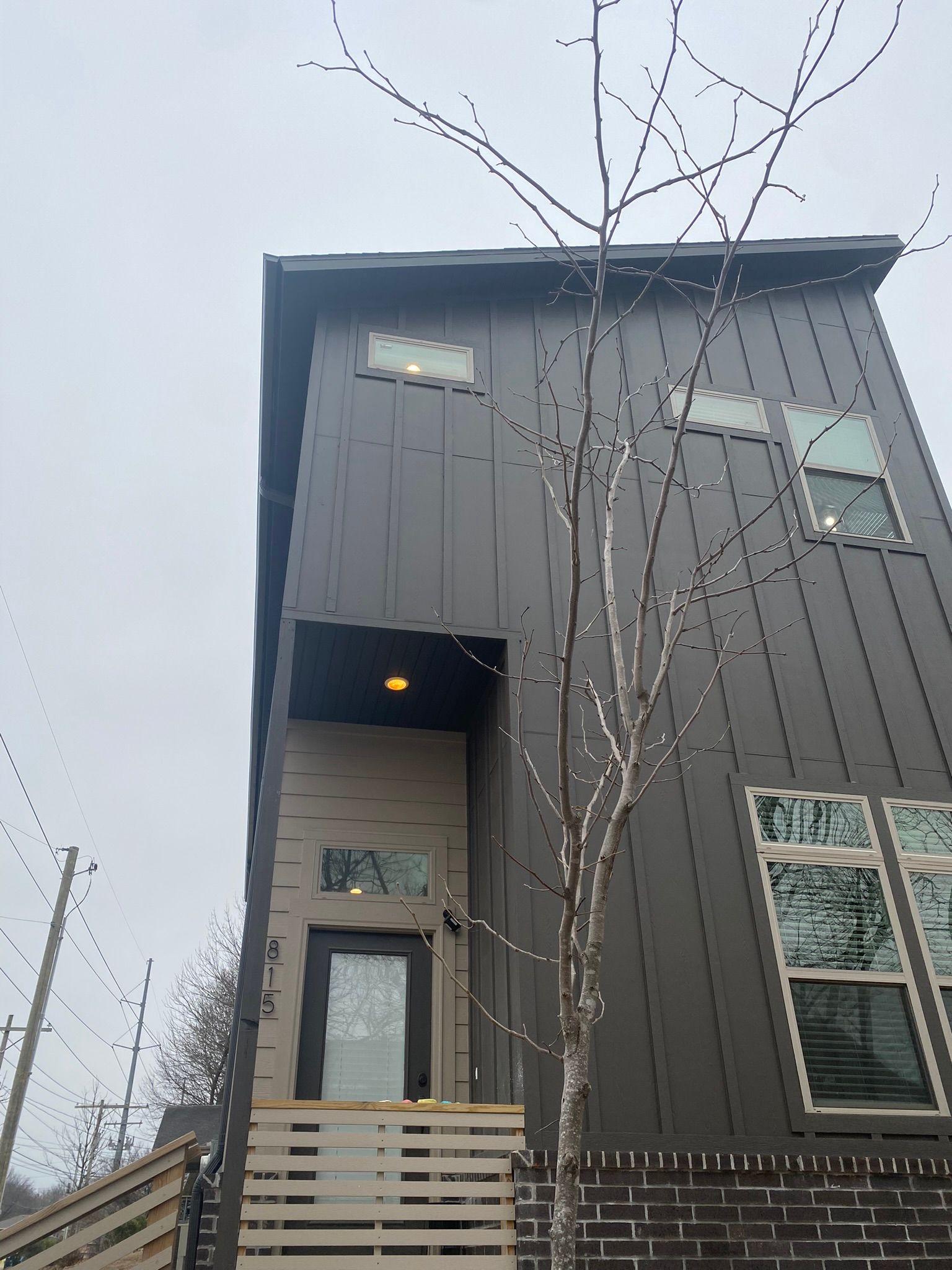 Modern three-story house with dark gray siding, brick base, and front entrance under a covered porch.
