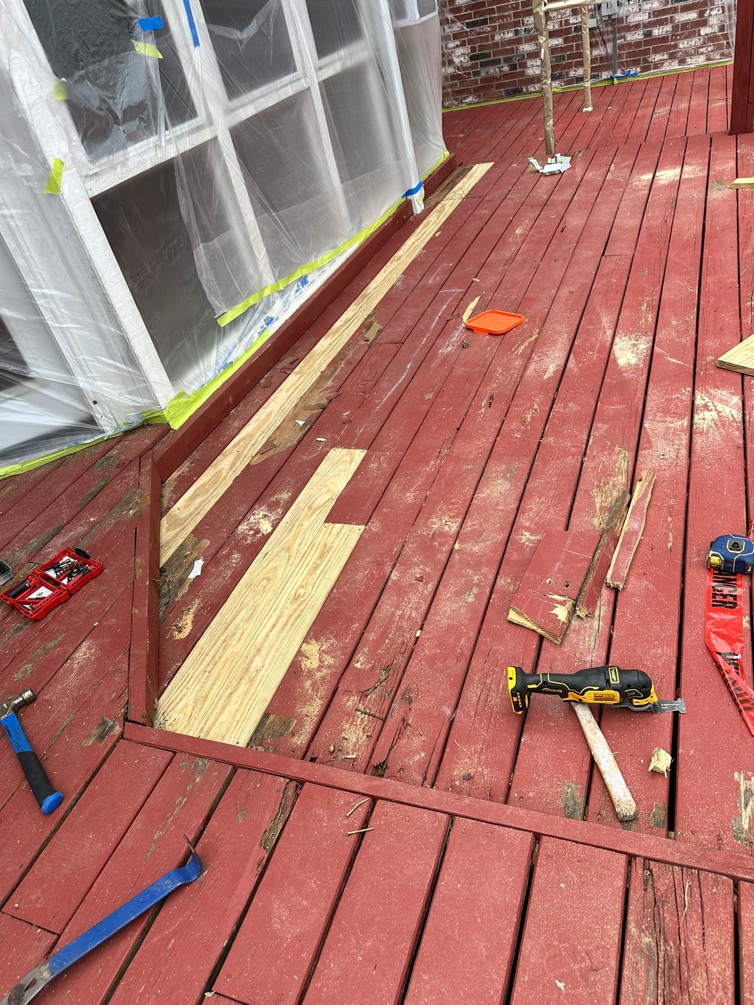 Deck renovation in progress; red wooden boards partially removed, tools scattered.