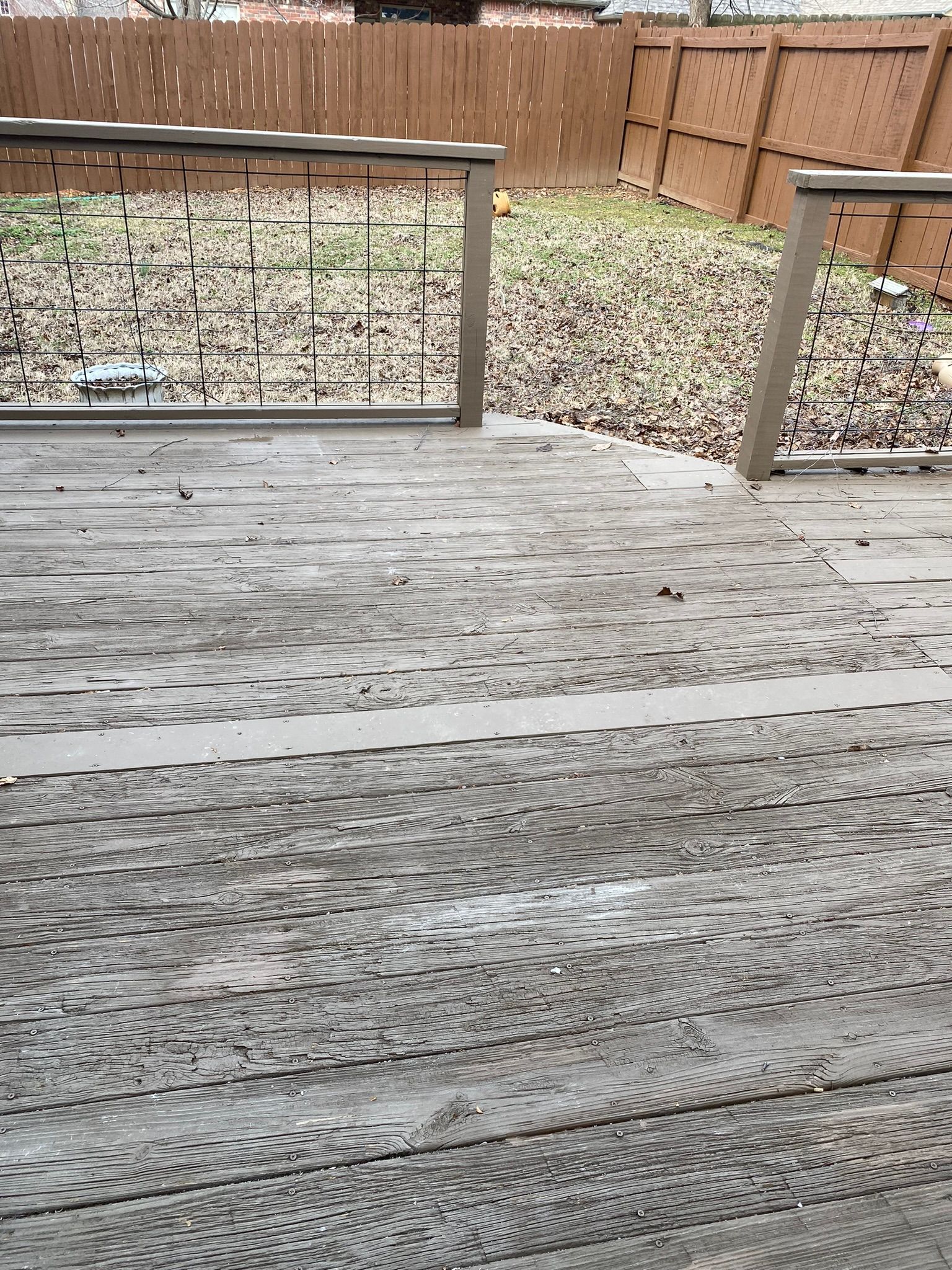 Wooden deck with weathered planks leading to a backyard with a brown fence and fallen leaves.