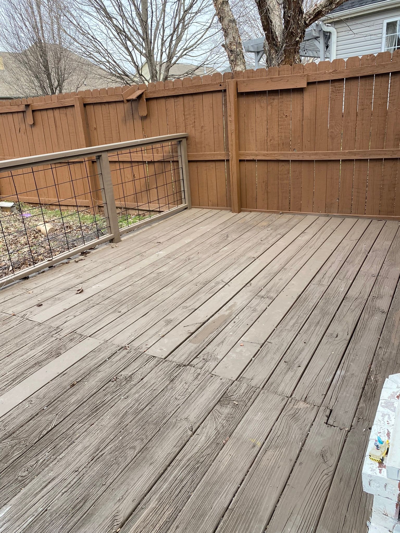 Wooden deck with peeling paint, surrounded by a brown fence.