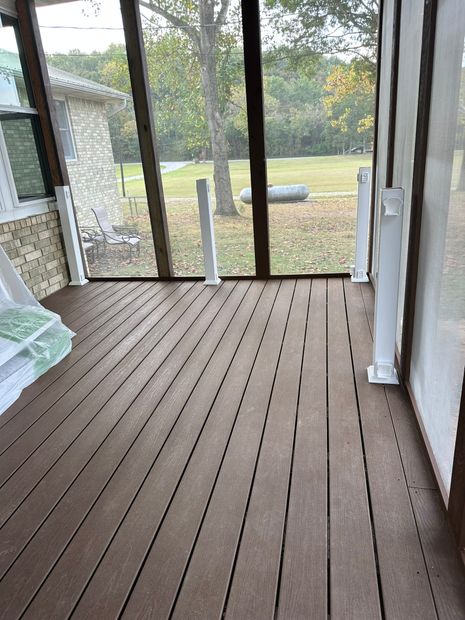 Brown wood deck on a screened porch. White posts frame the view of a grassy yard with trees and an inflatable pool.