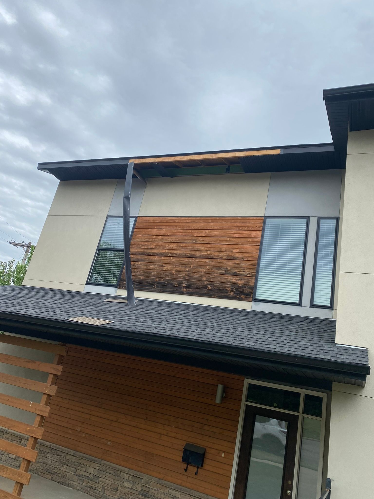 Modern two-story house with damaged wooden facade and roof, under cloudy sky.
