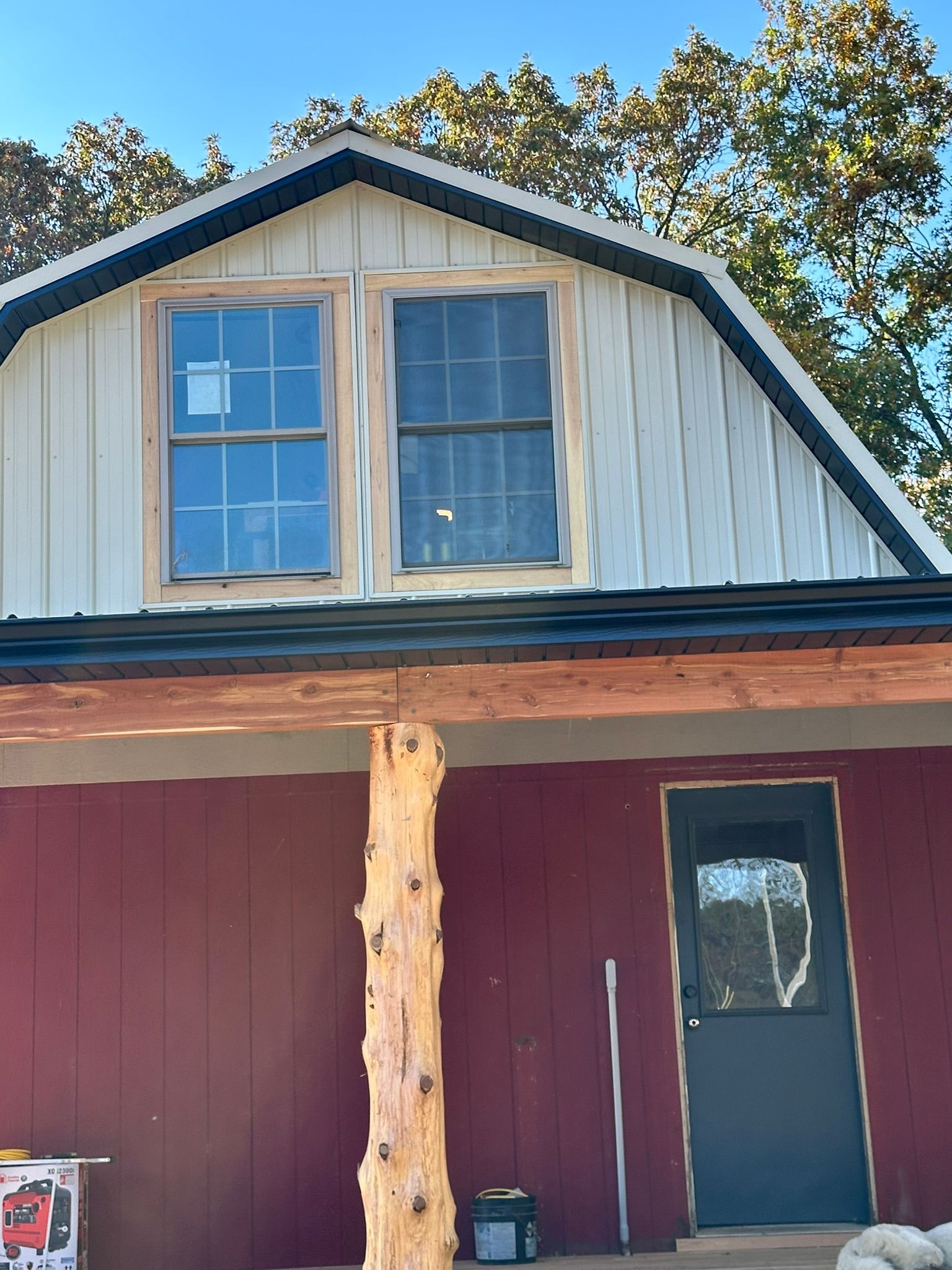 Red and white building with two windows in the loft, a log column, and a black door.