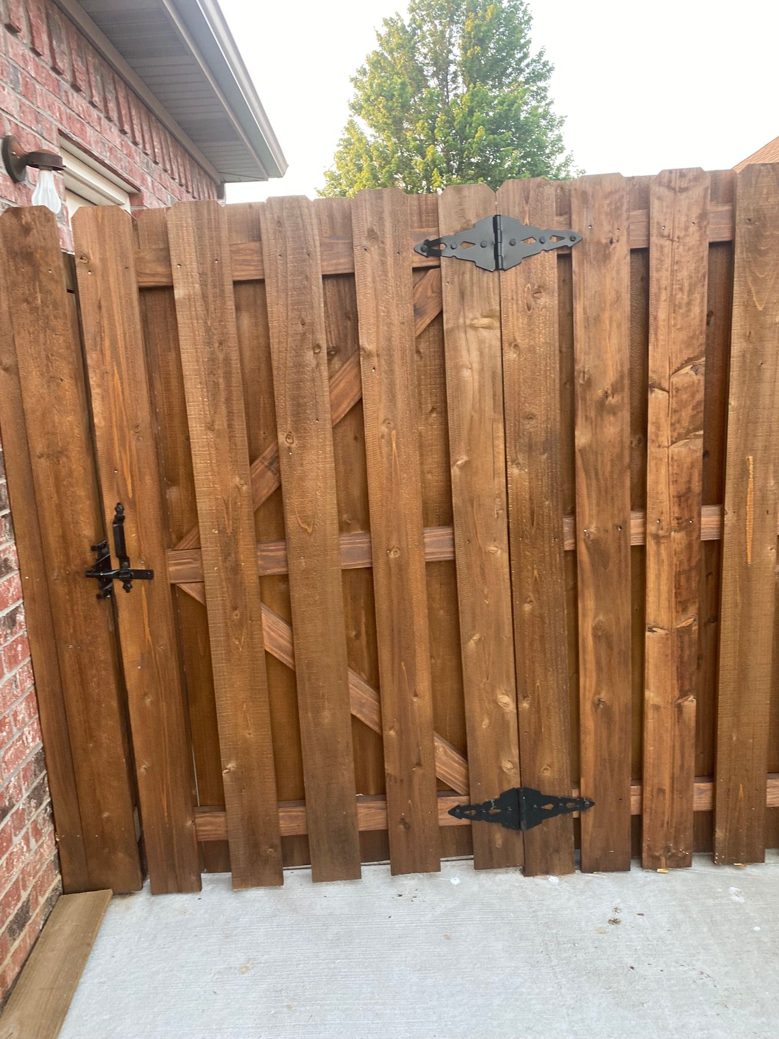 Wooden gate with black hinges and latch, attached to brick wall.