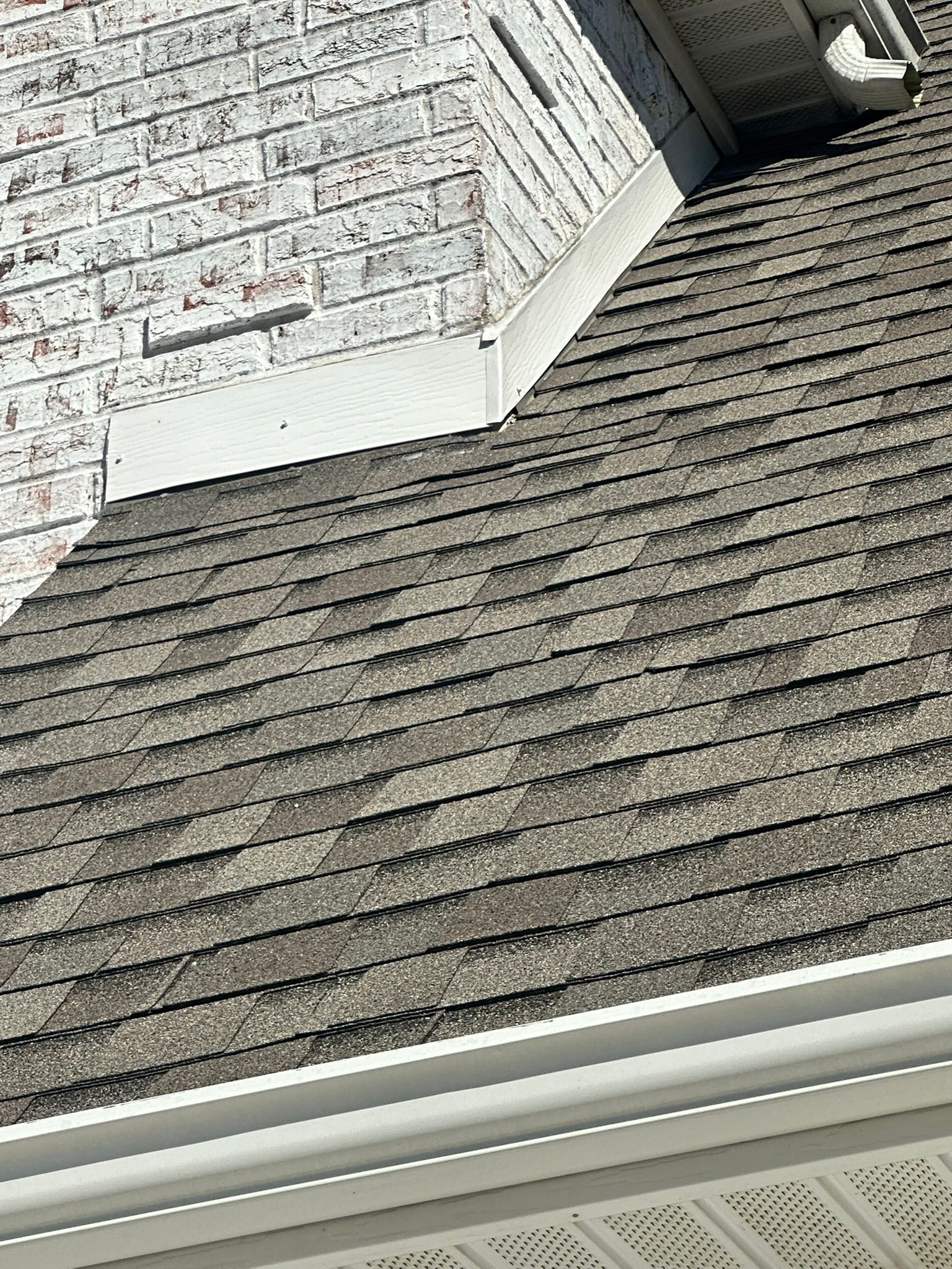 Gray asphalt shingle roof next to a white brick wall. White gutter and trim along bottom edge.