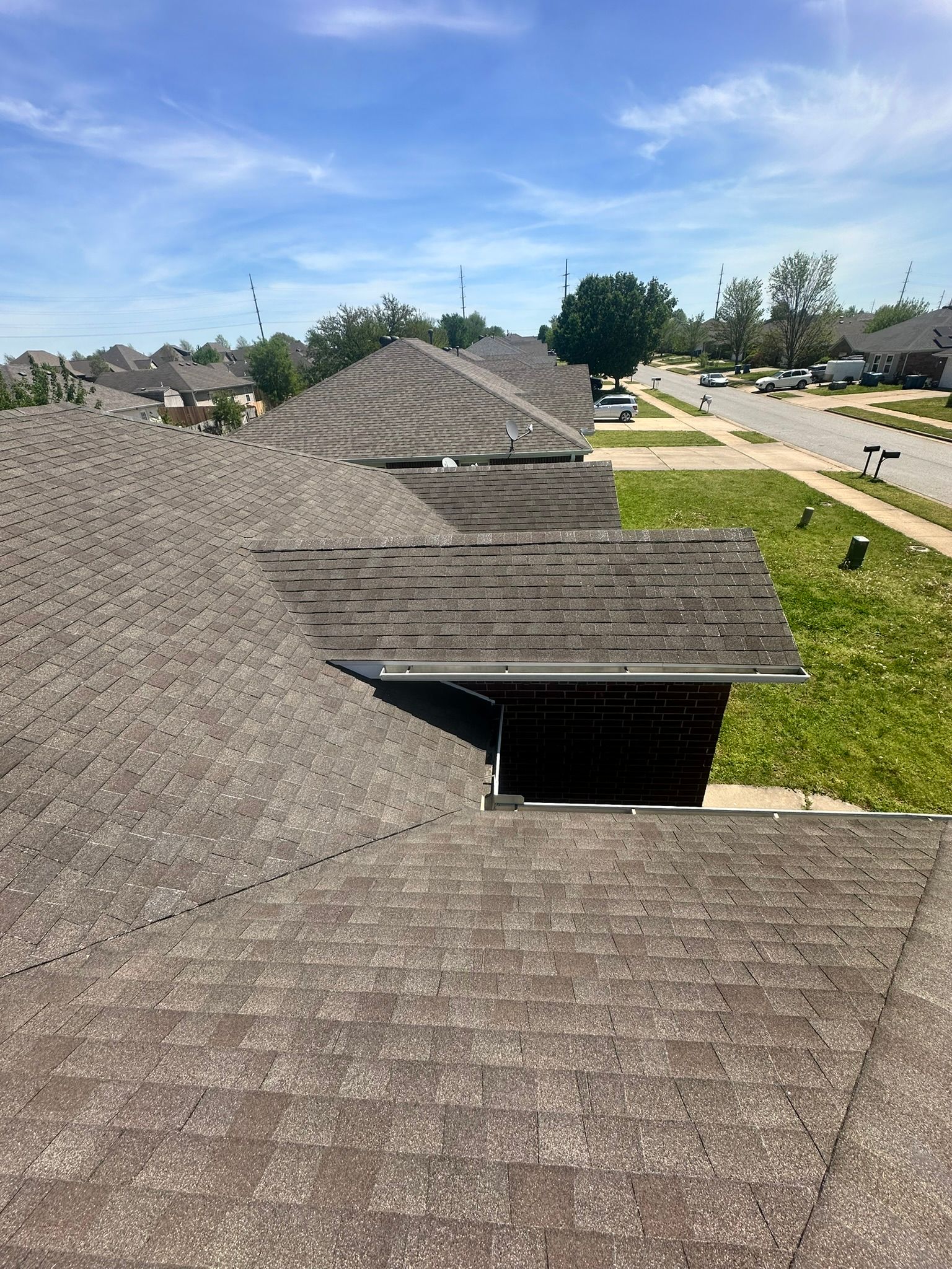 View of a house roof from above, with several adjacent roofs in a suburban area, under a blue sky.