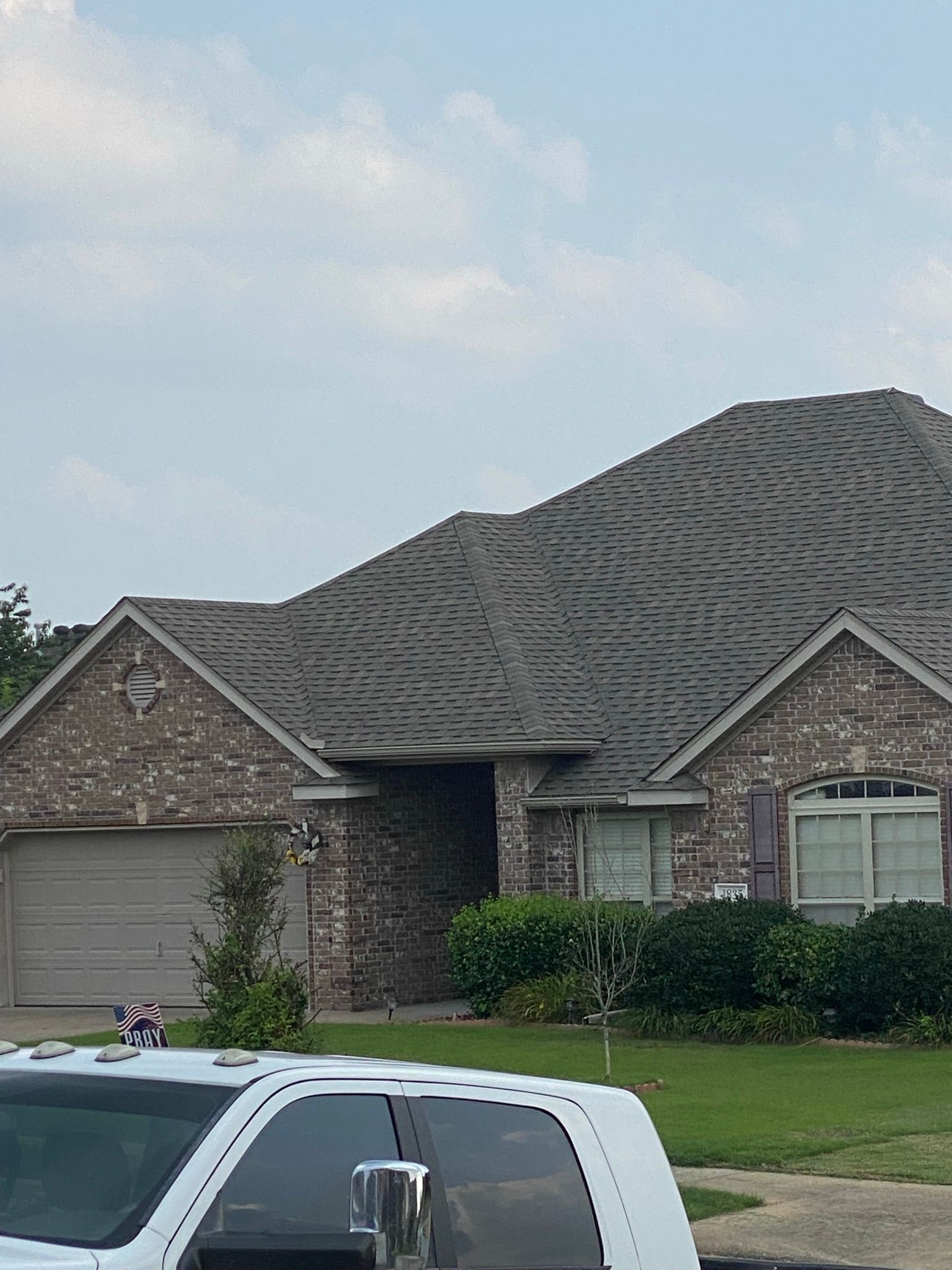 Brick house with a gray roof and a garage door, under a cloudy sky.