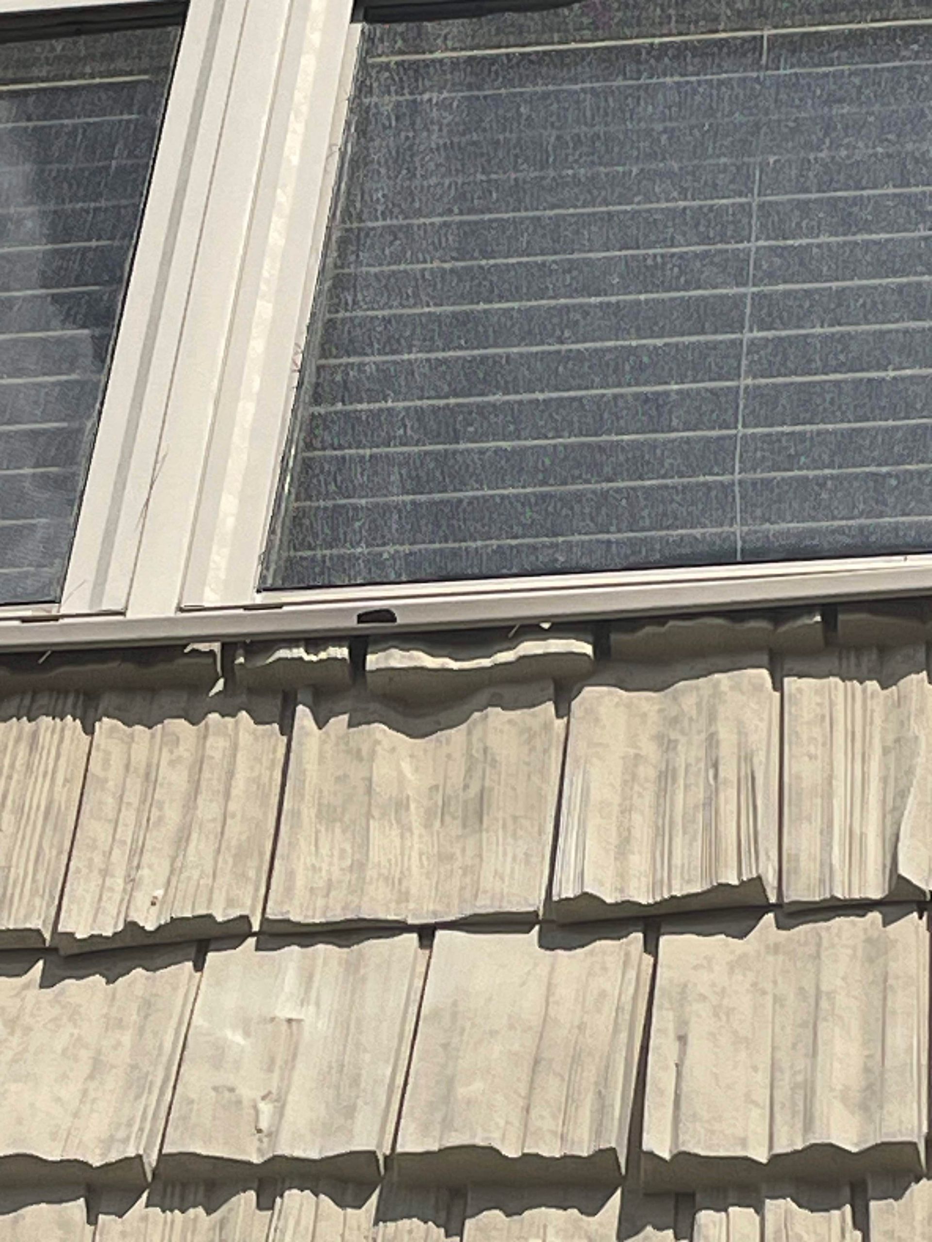 Window above weathered wood shingles. Gray frames and window blinds.