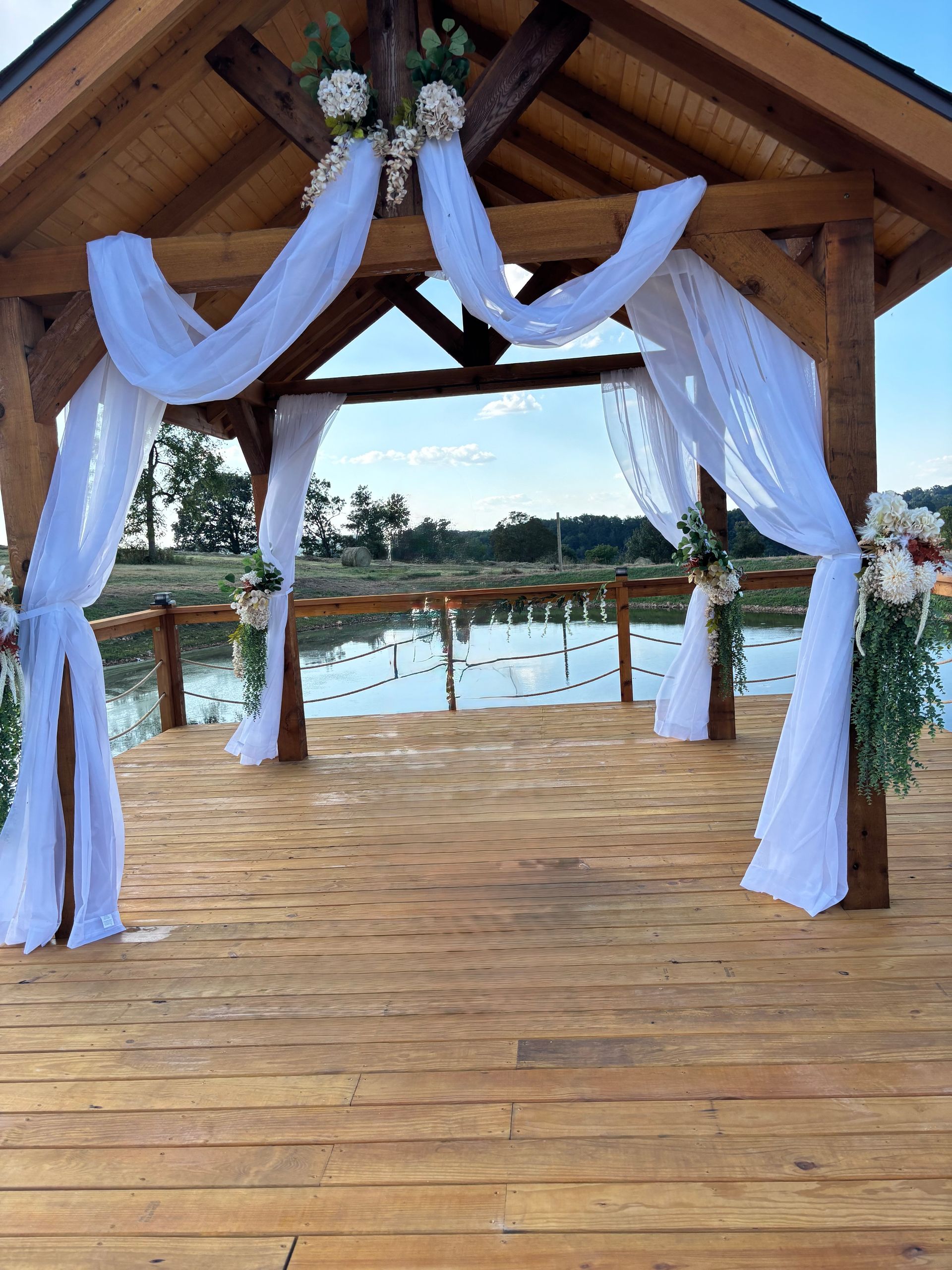 Wooden gazebo decorated for an event, overlooking water with a clear sky in the background.