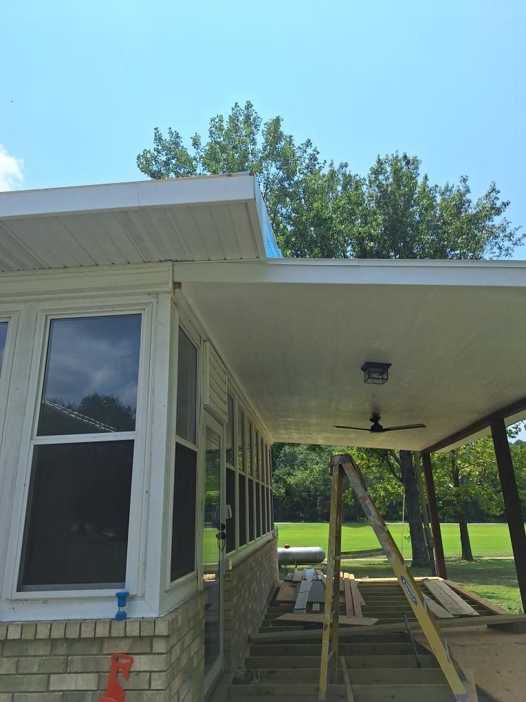 Porch with windows, brick, and ladder against the support beams; trees and sky in the background.