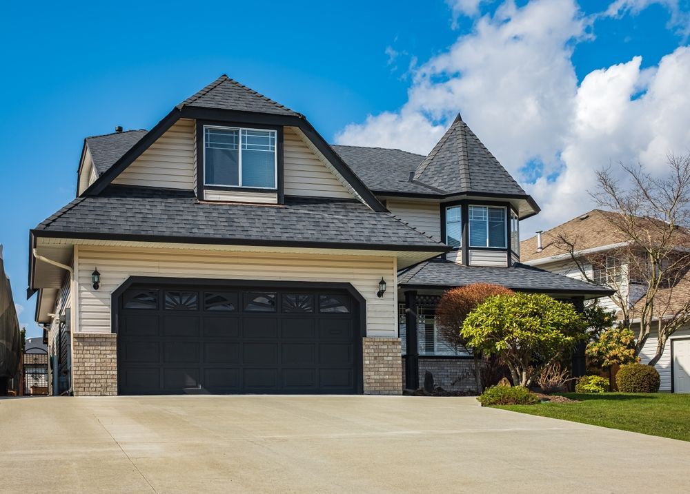 Tan house with black roof, garage door, and turret, on a sunny day.