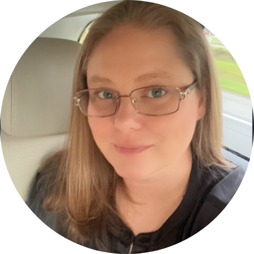 Woman with glasses in car, looking at the camera.