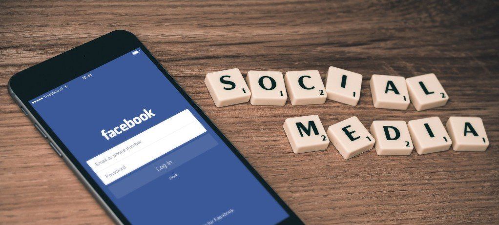 A cell phone is sitting on a wooden table next to scrabble tiles that say social media.