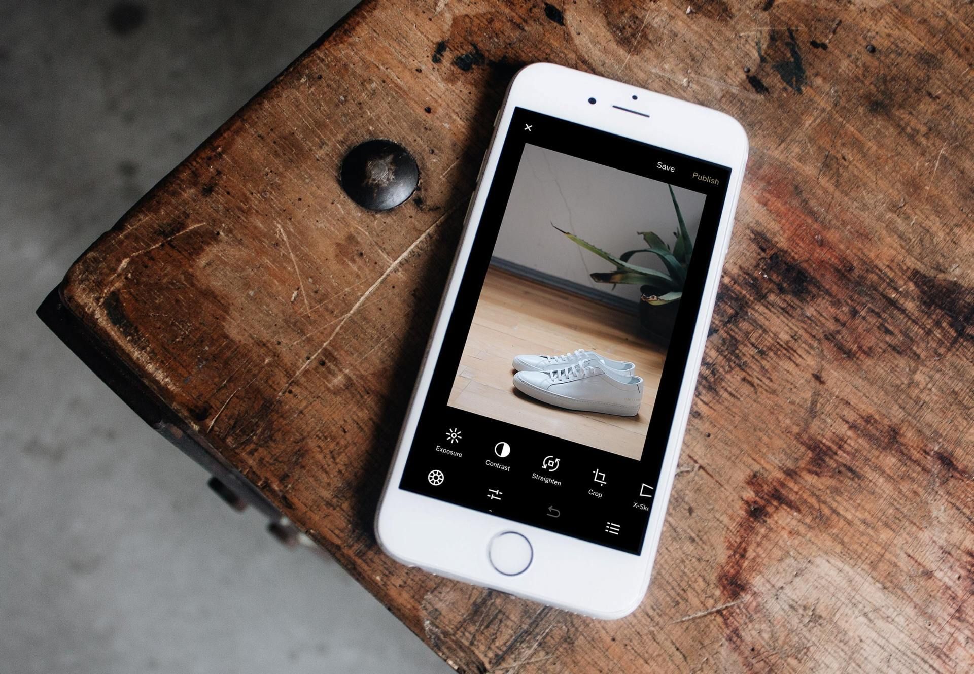 A cell phone is taking a picture of a plant on a wooden table.