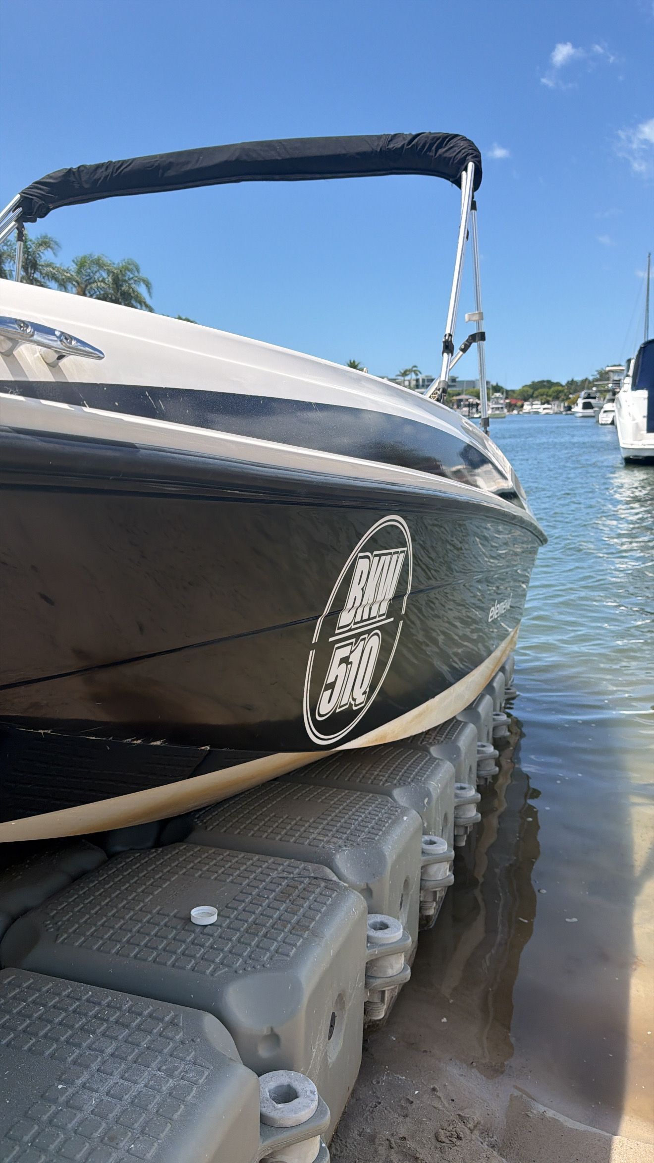 A black and white boat docked on a grey floating platform in a sunny, clear-water waterway.