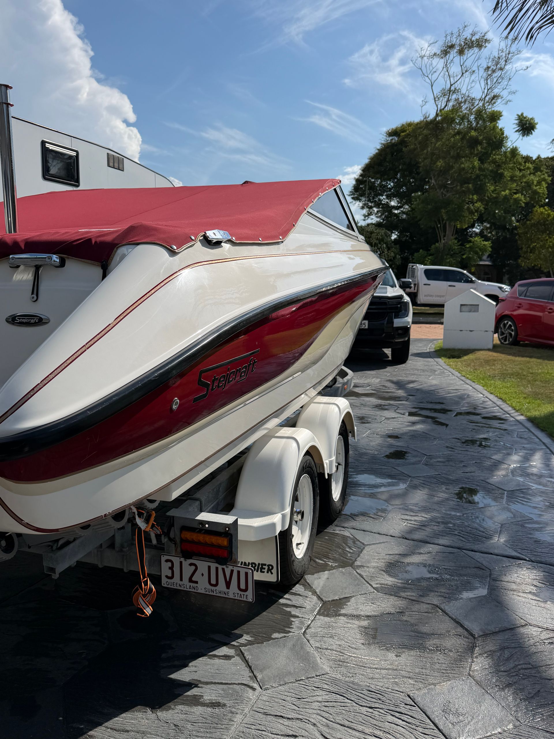 A red and white boat on a trailer parked in a driveway on a sunny day.