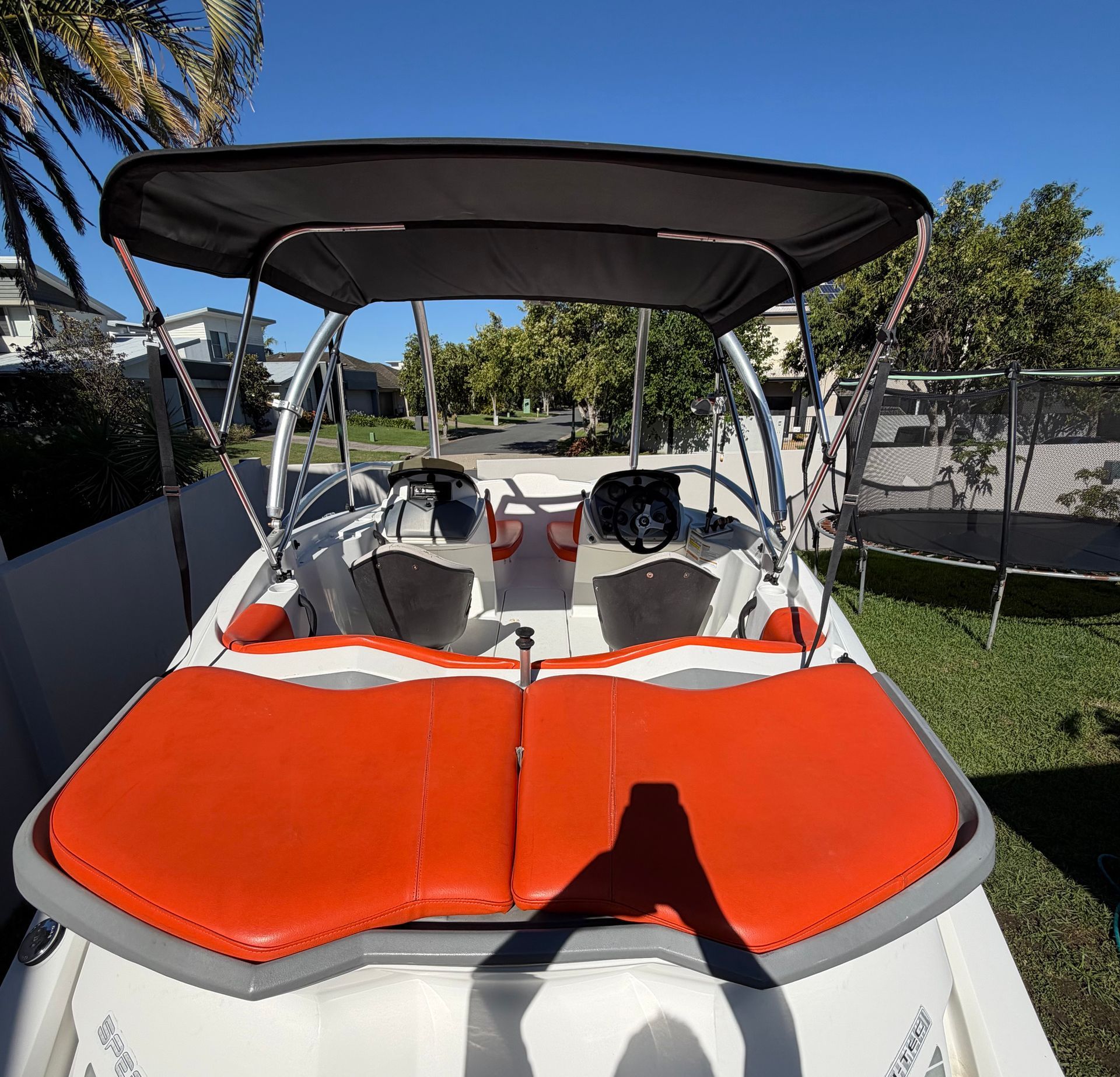 A boat with orange cushioned seats and a black bimini top, parked on a grassy area during the day.