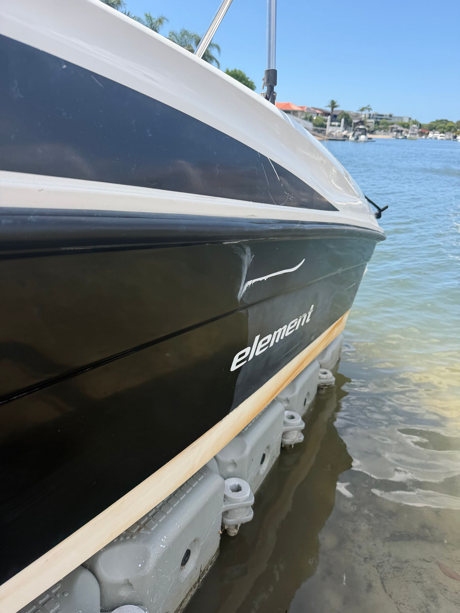 A close-up view of a black boat hull docked against white plastic floating modules on a sunny day.