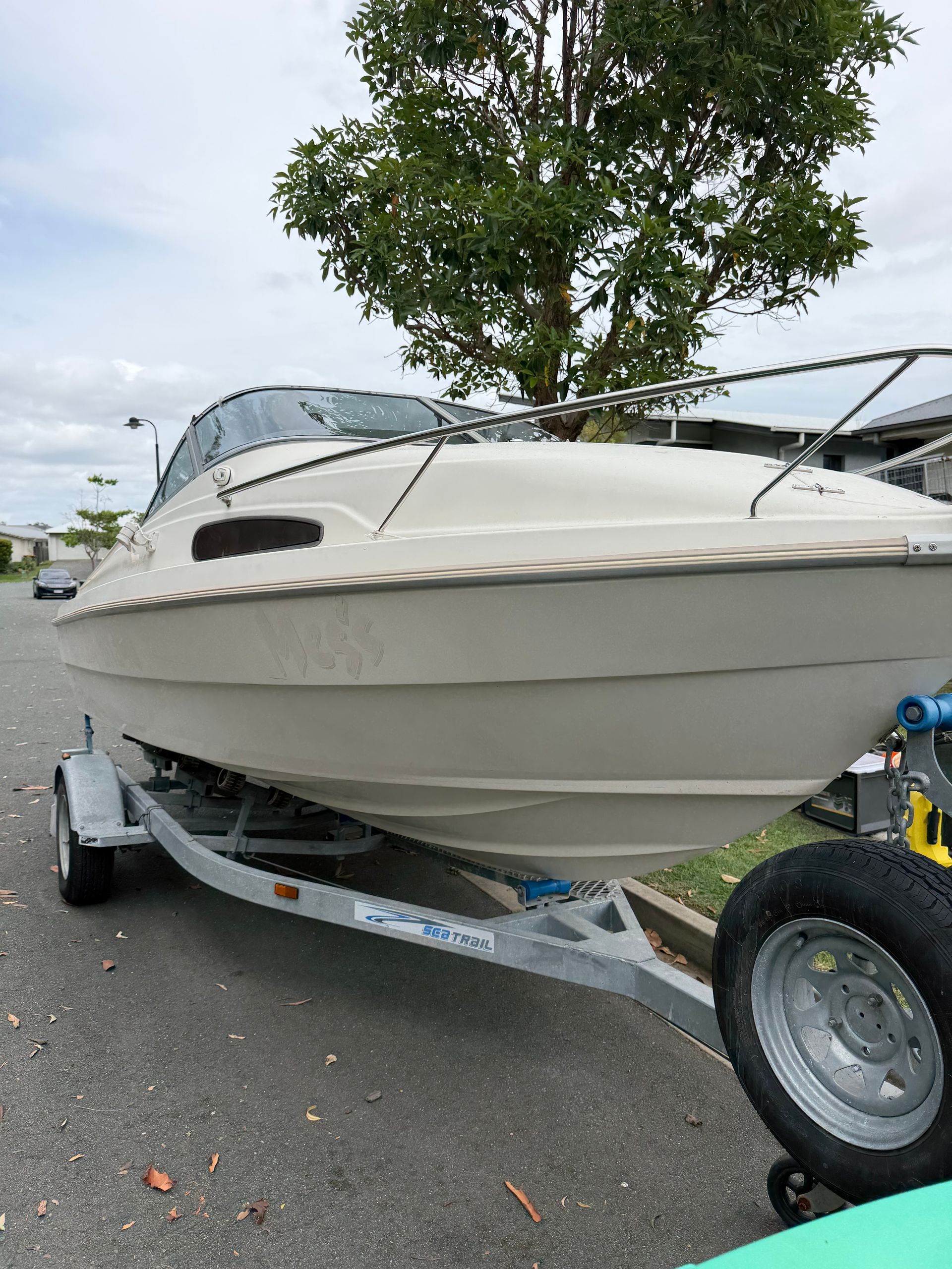 A light-colored cabin cruiser boat on a trailer parked outdoors on an asphalt surface.