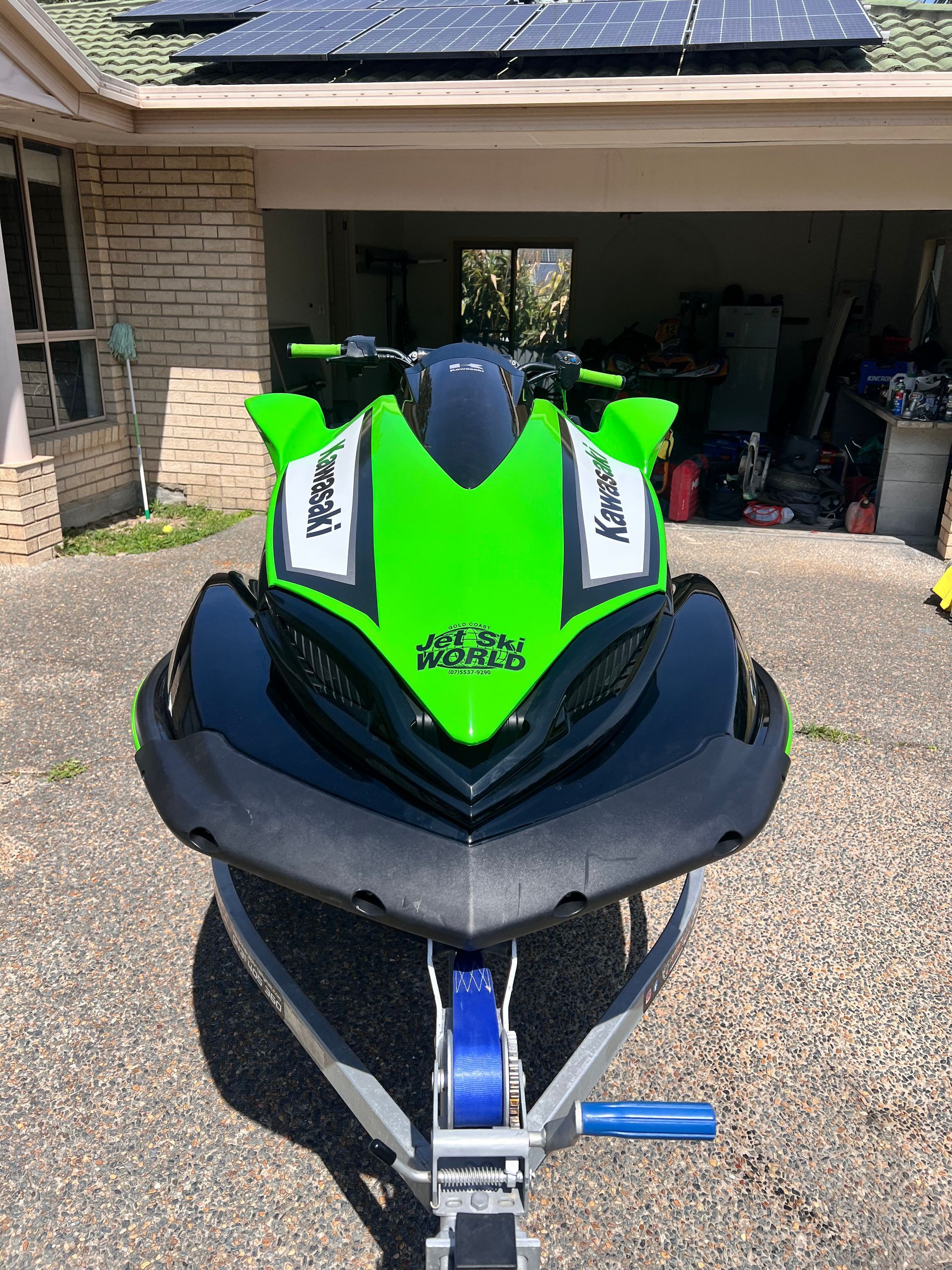 A bright green and black Kawasaki jet ski sits on a trailer in a residential driveway.