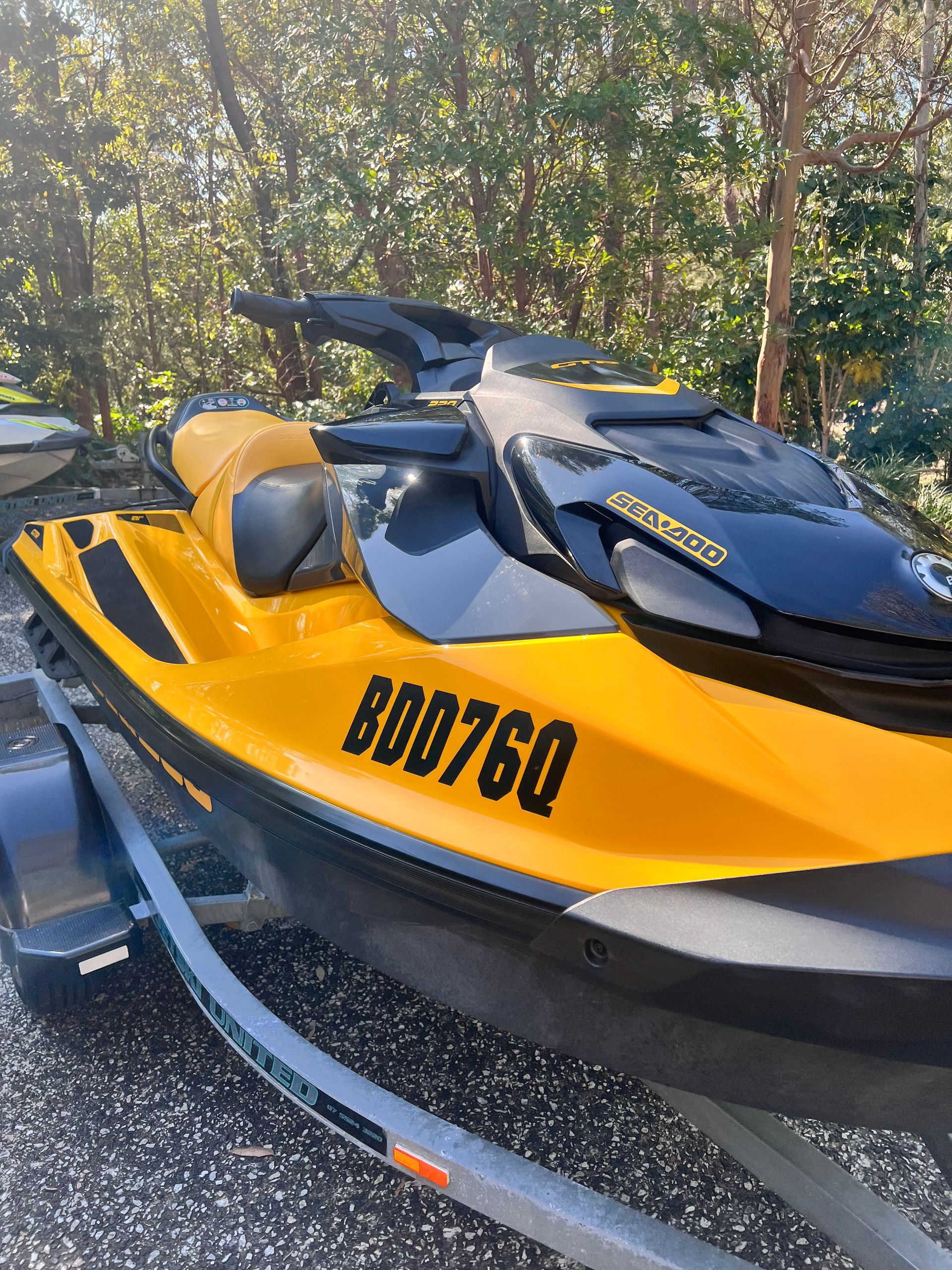 A yellow and black Sea-Doo personal watercraft with registration number BDD76Q, parked on a trailer outdoors.