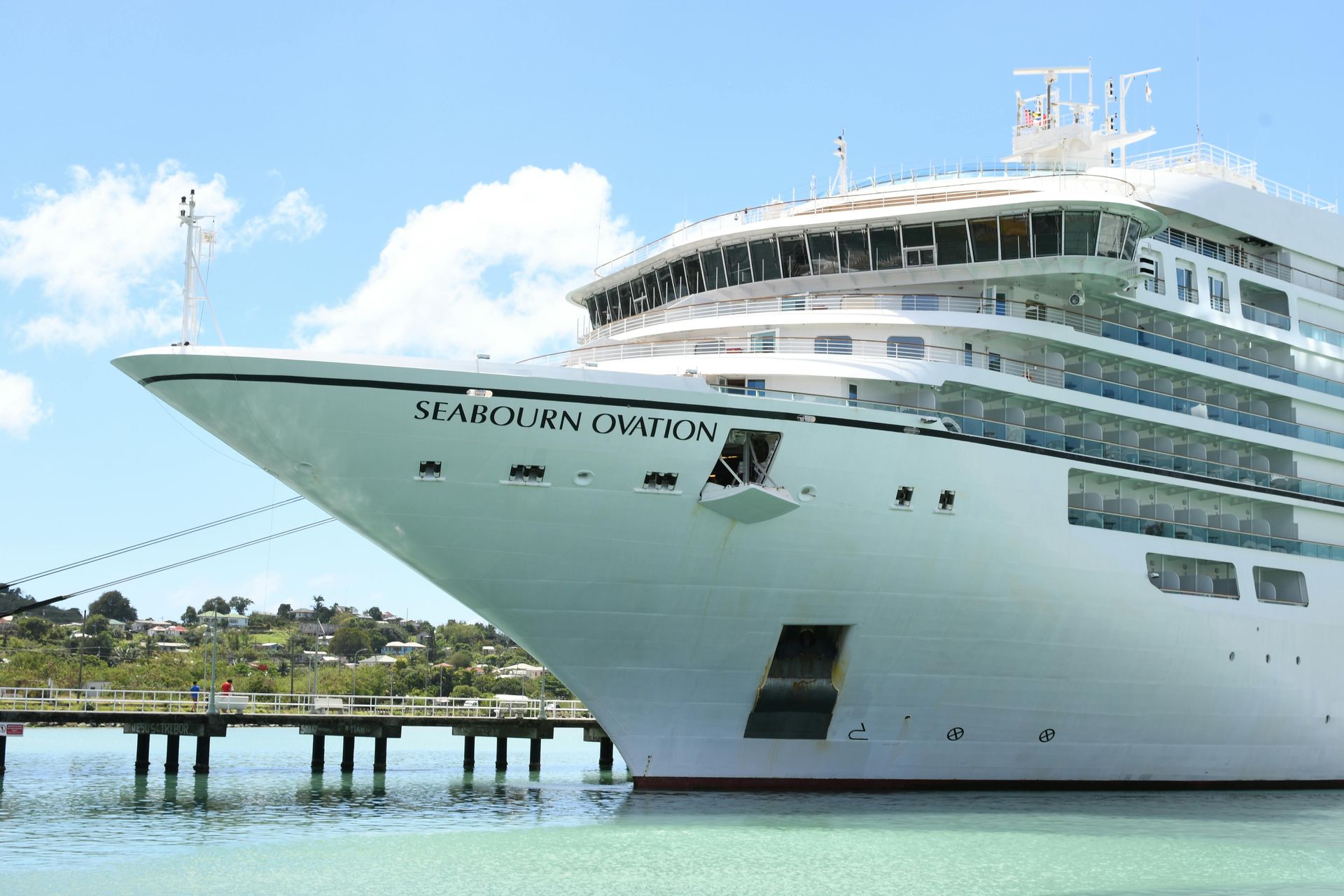 The cruise ship Seabourn Ovation docked at a pier under a bright, partly cloudy blue sky.